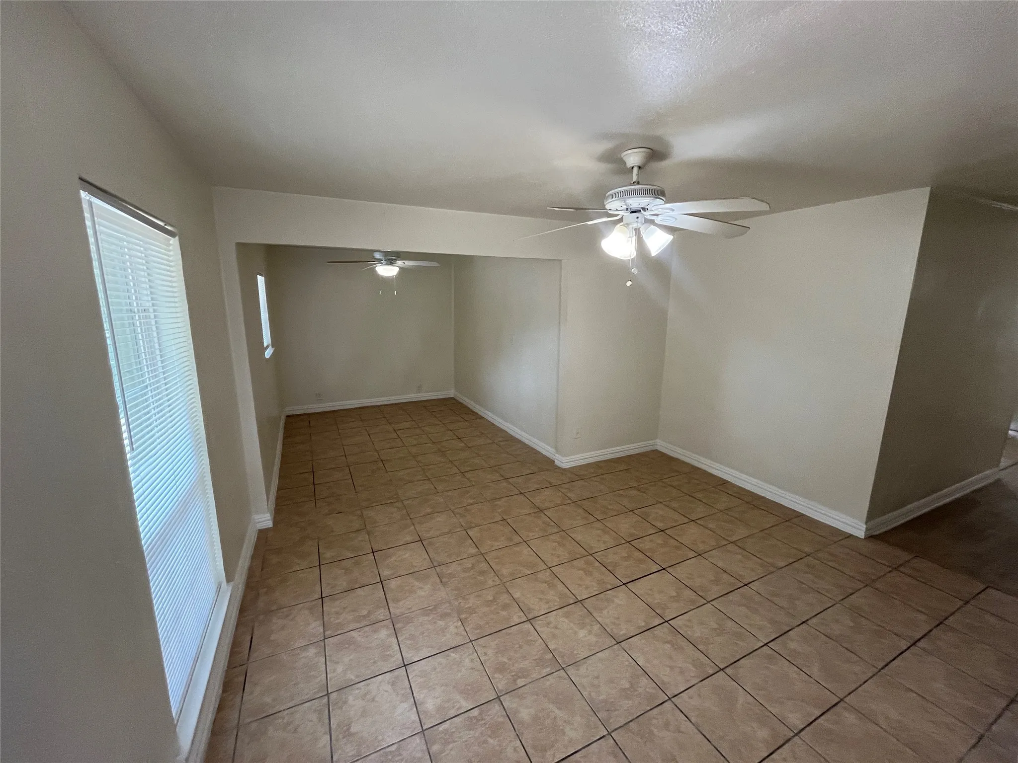 Tile flooring, multiple windows with blinds, and two ceiling fans with integrated lighting