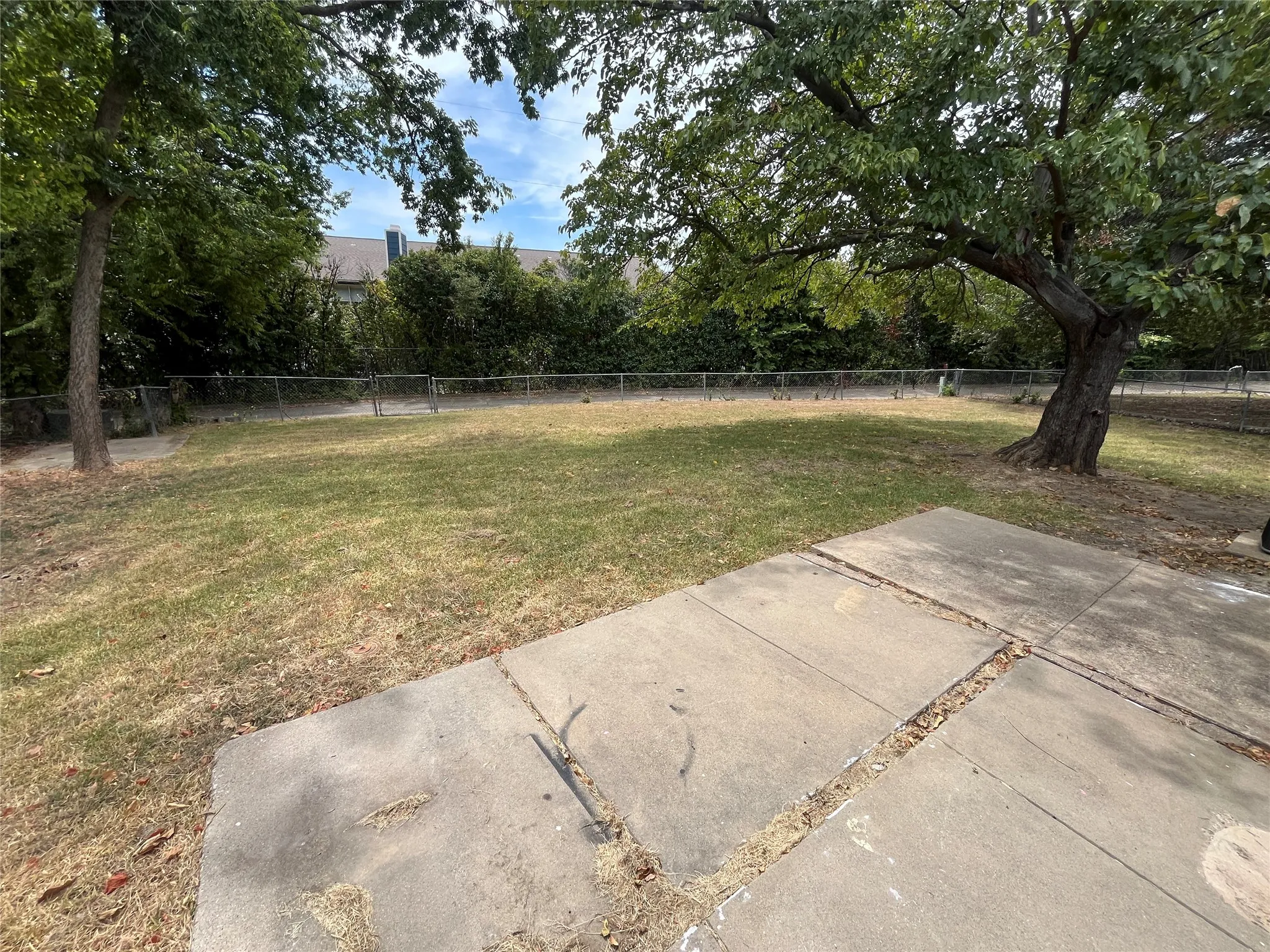 Expansive grass area featuring mature trees and a chain-link fence
