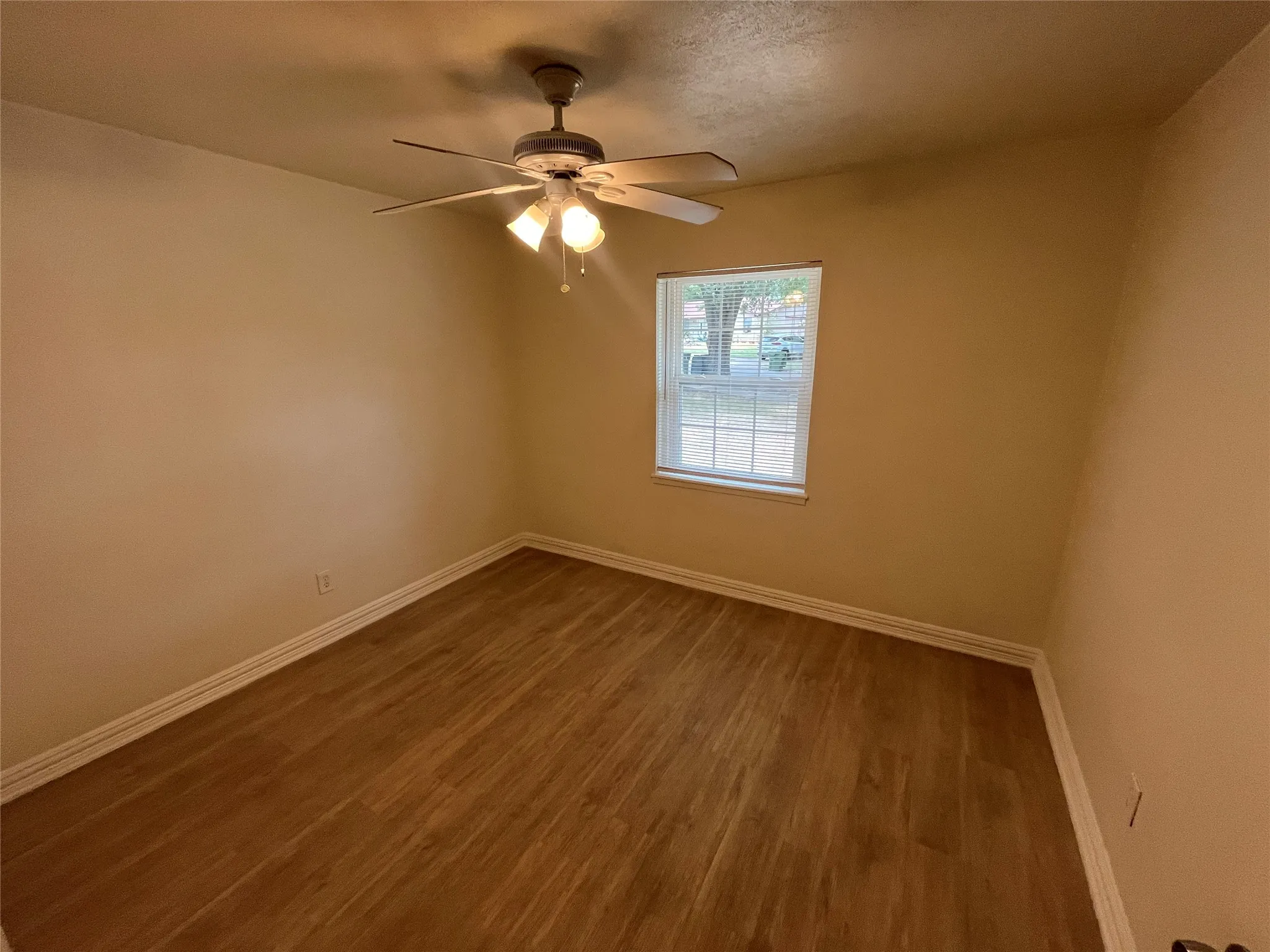 Wood-finish flooring, neutral wall tones, ceiling fan with integrated lighting, and a multi-pane window