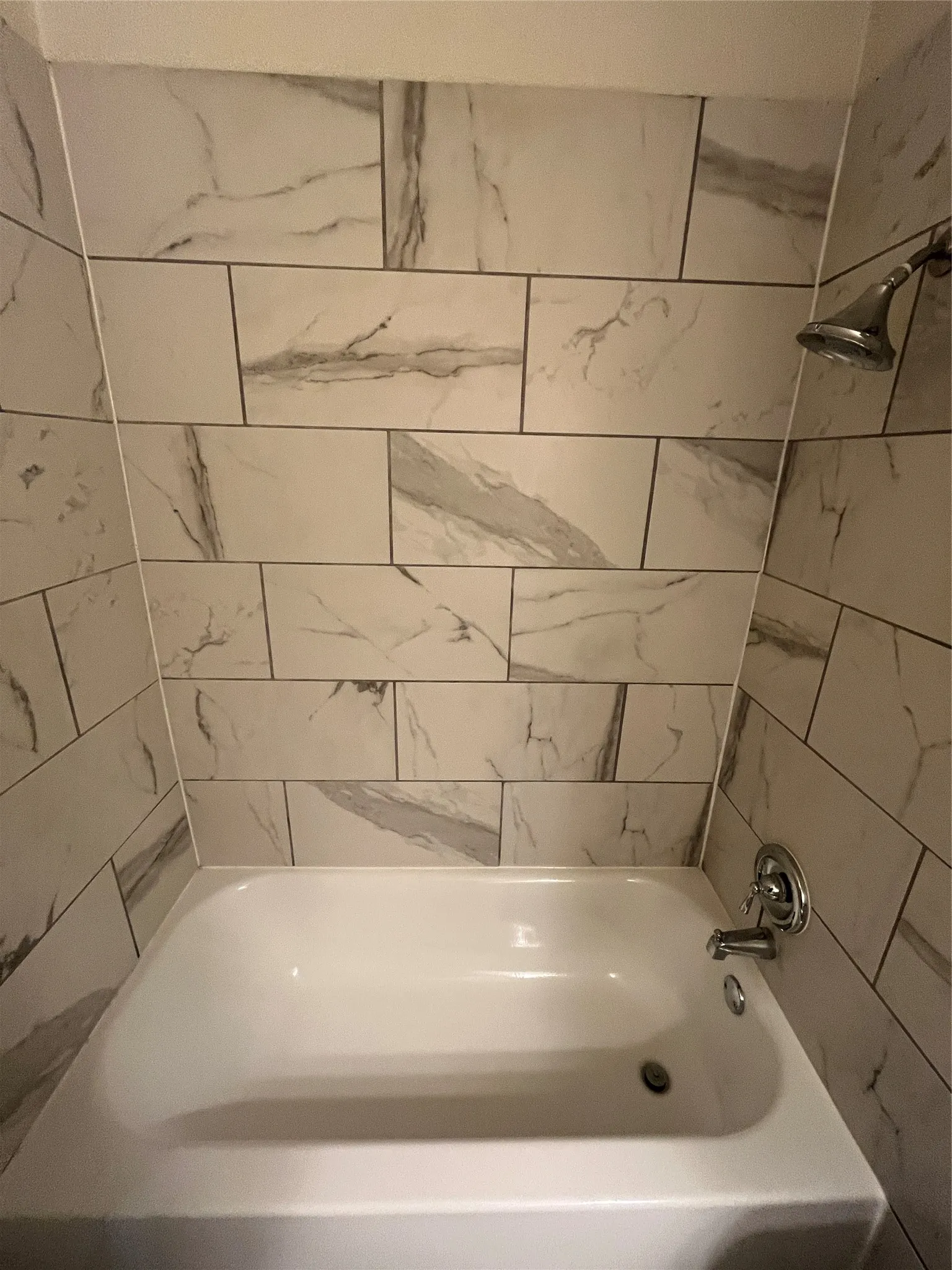 White porcelain bathtub with chrome fixtures and white tiled surround featuring grey veining