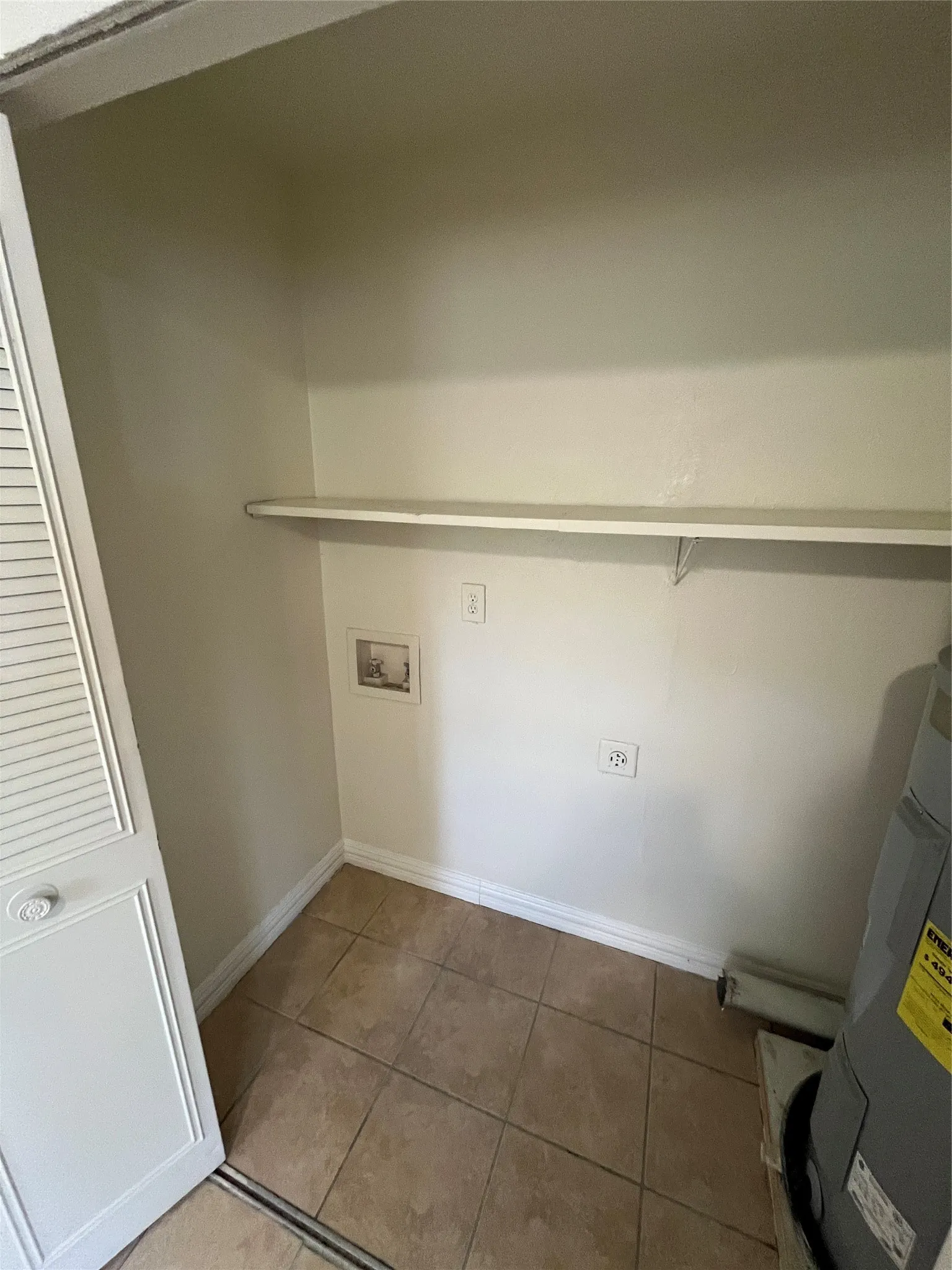 Utility closet featuring a tiled floor, built-in shelving, and louvered bi-fold doors