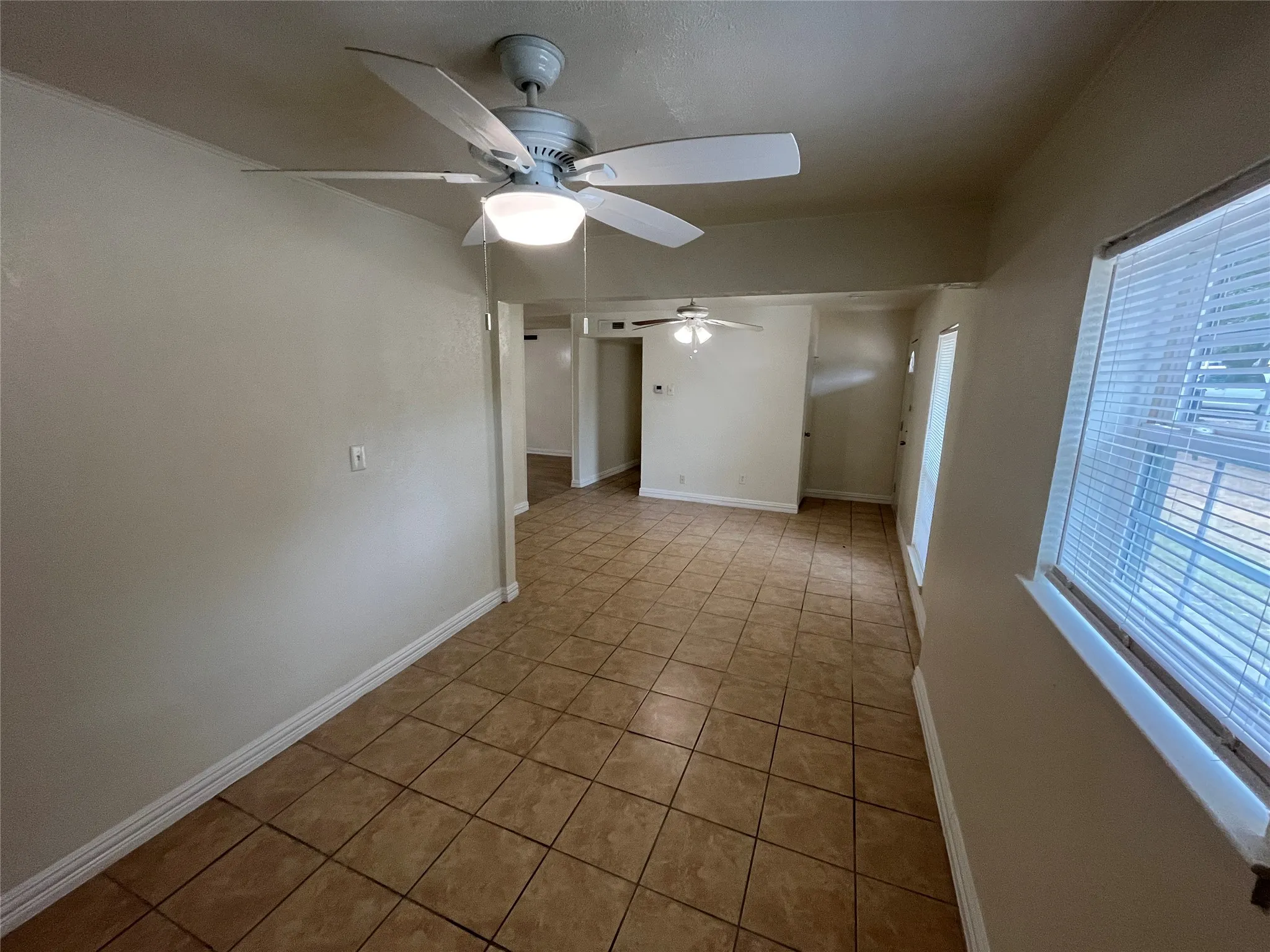 Tile flooring, ceiling fan with integrated lighting, window with blinds, neutral wall tones, and white trim