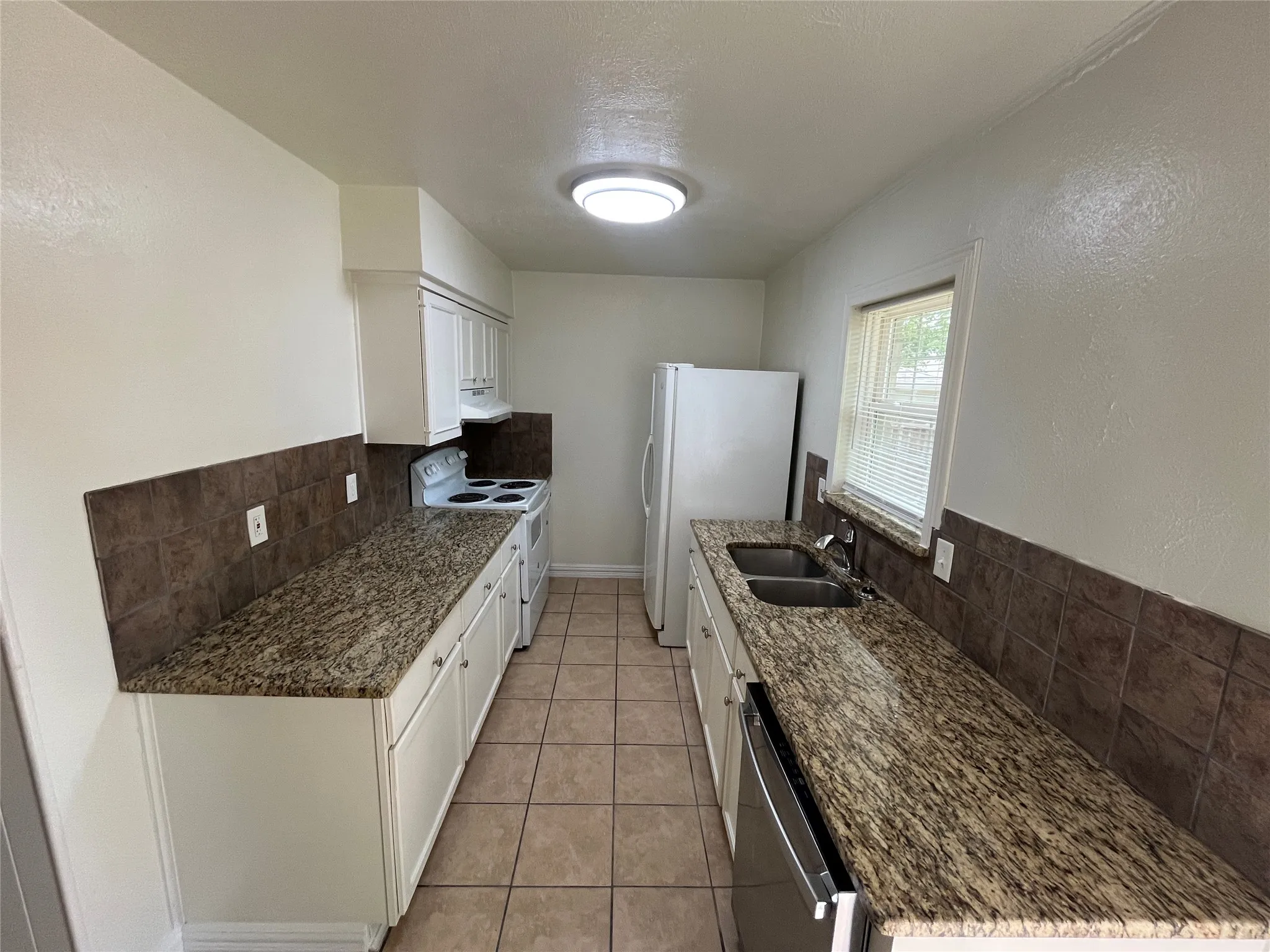 Kitchen featuring tile flooring, white cabinetry, a dual-basin stainless steel sink, and a window with blinds