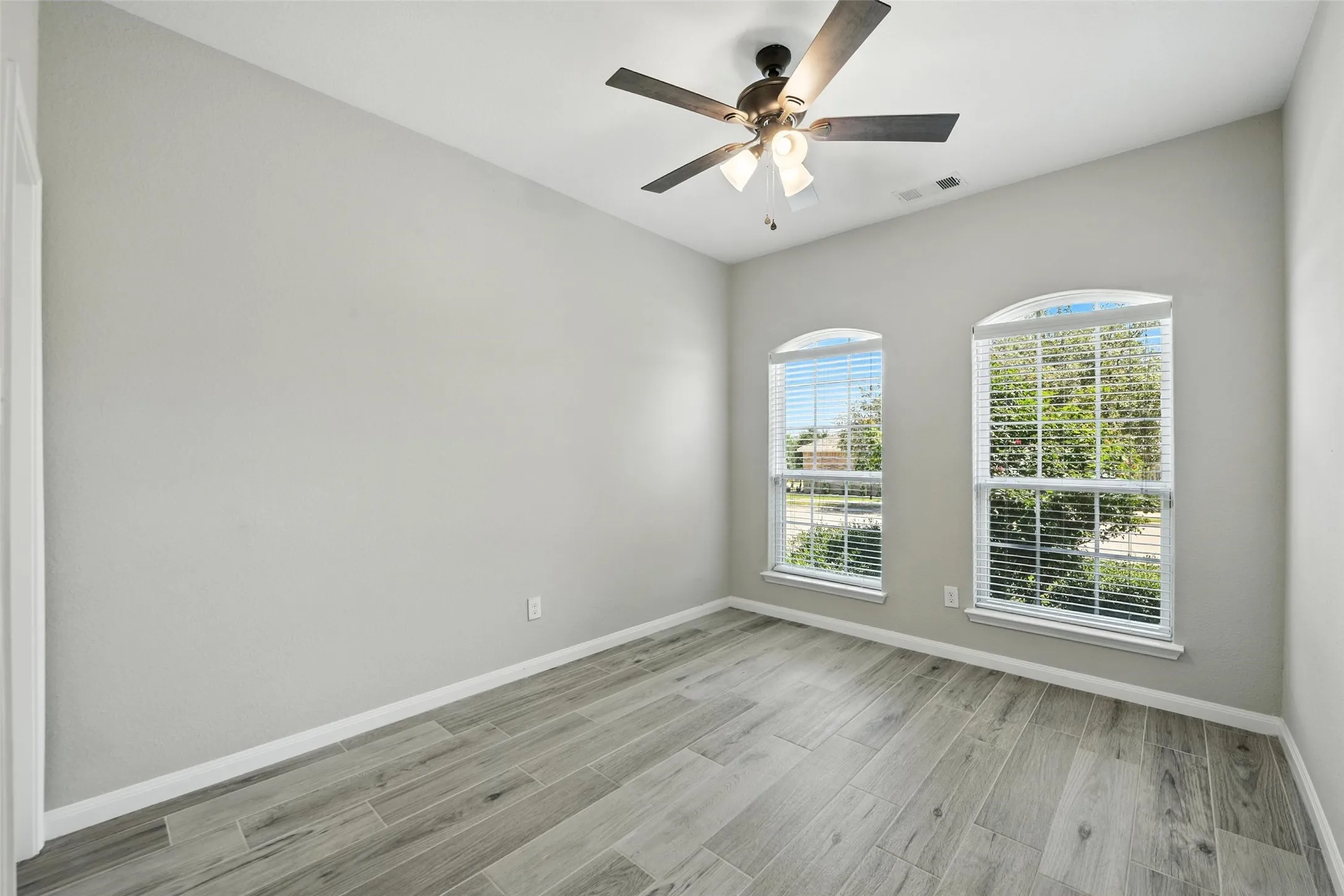 Vaulted ceiling featuring a ceiling fan with integrated lighting, two arched windows with blinds, and wood-finish flooring in the secondary bedroom