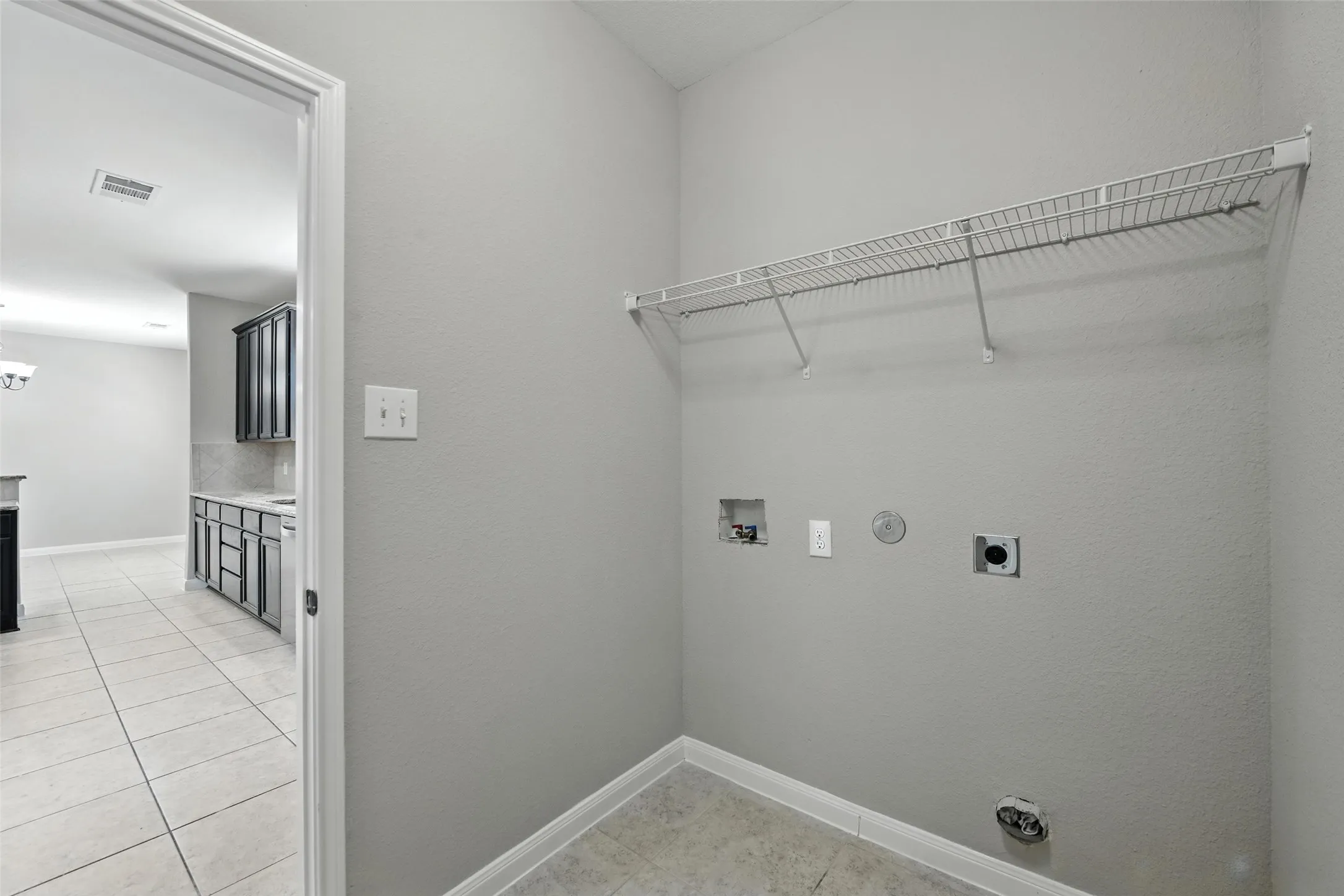 Laundry area with a wire storage shelf, utility hookups, and tiled flooring