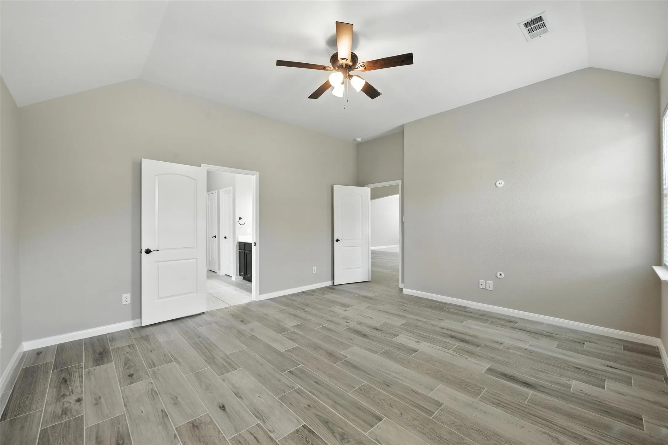 Vaulted ceiling featuring a ceiling fan with light fixture, wood-finish flooring, and white paneled doors