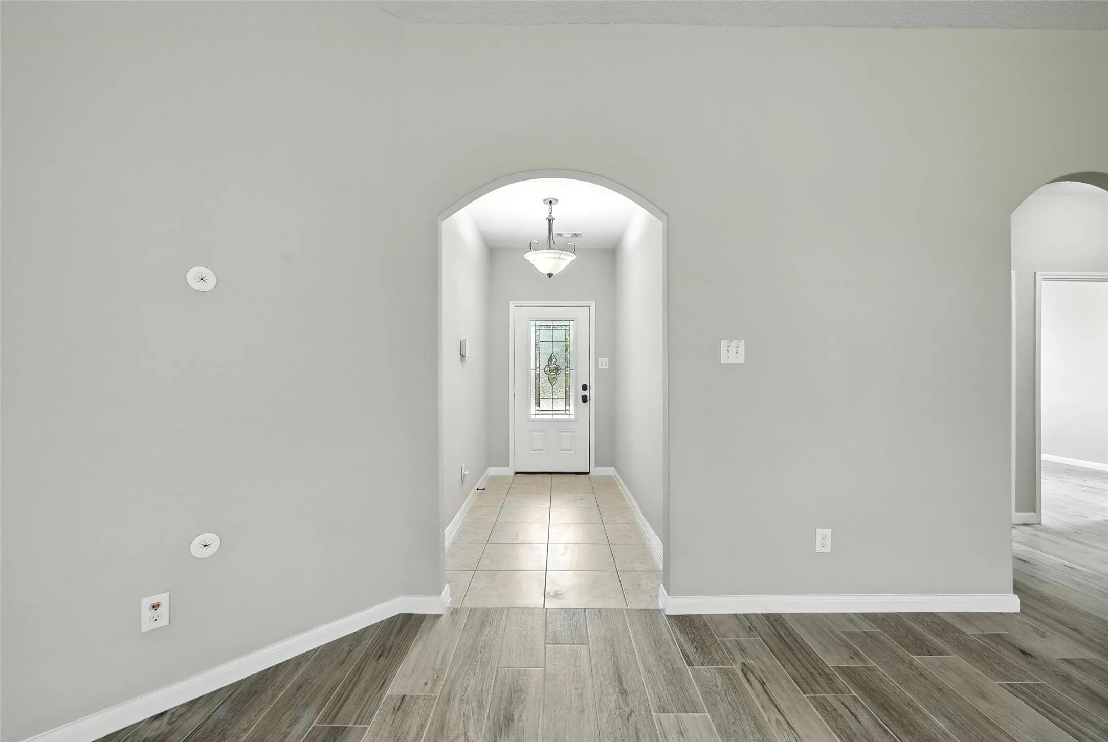 Archway entry with a front door featuring decorative glass, tile flooring, and wood-finish flooring