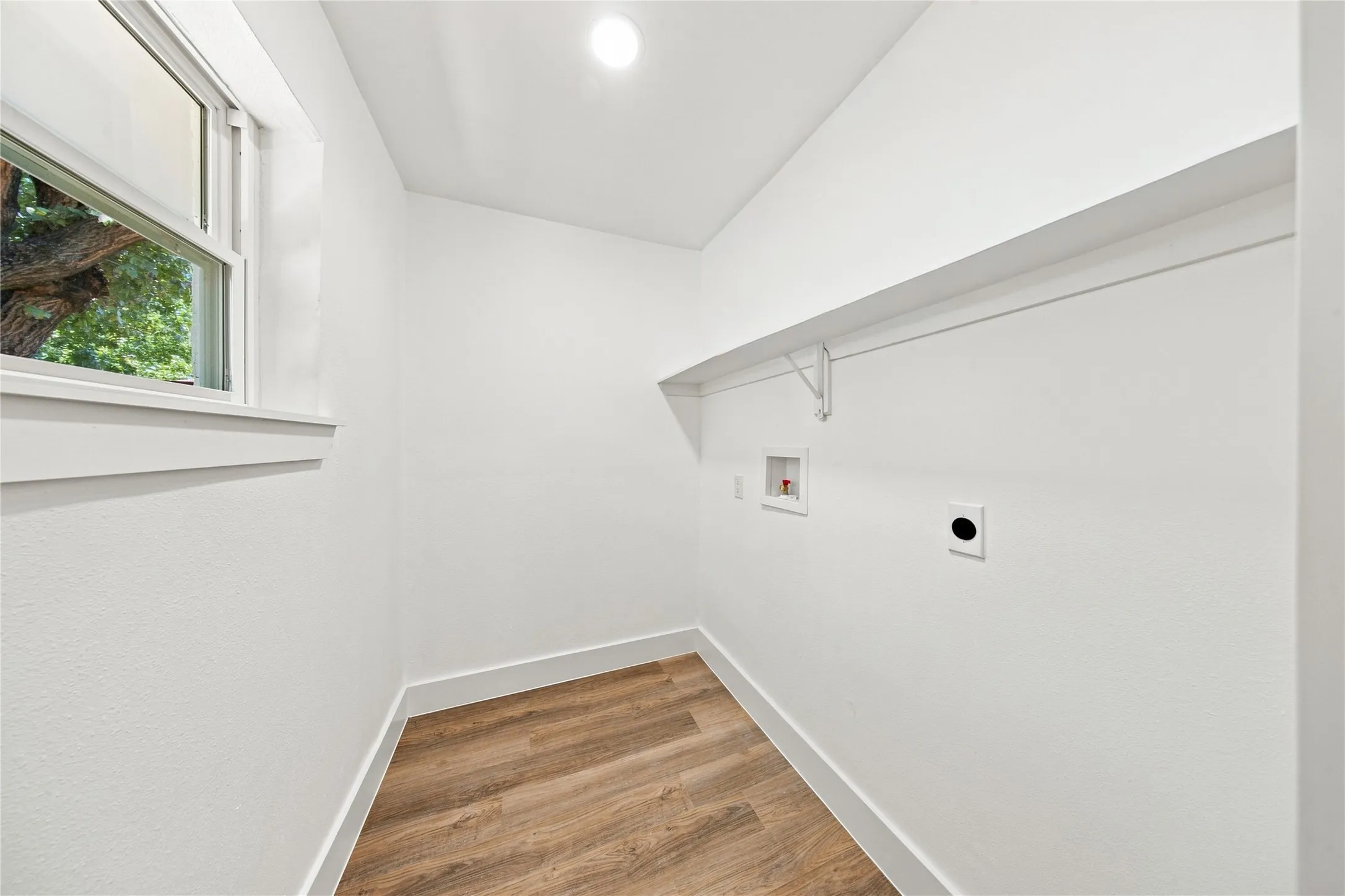 Utility space featuring wood-finish flooring, a window, overhead lighting, and an integrated shelf