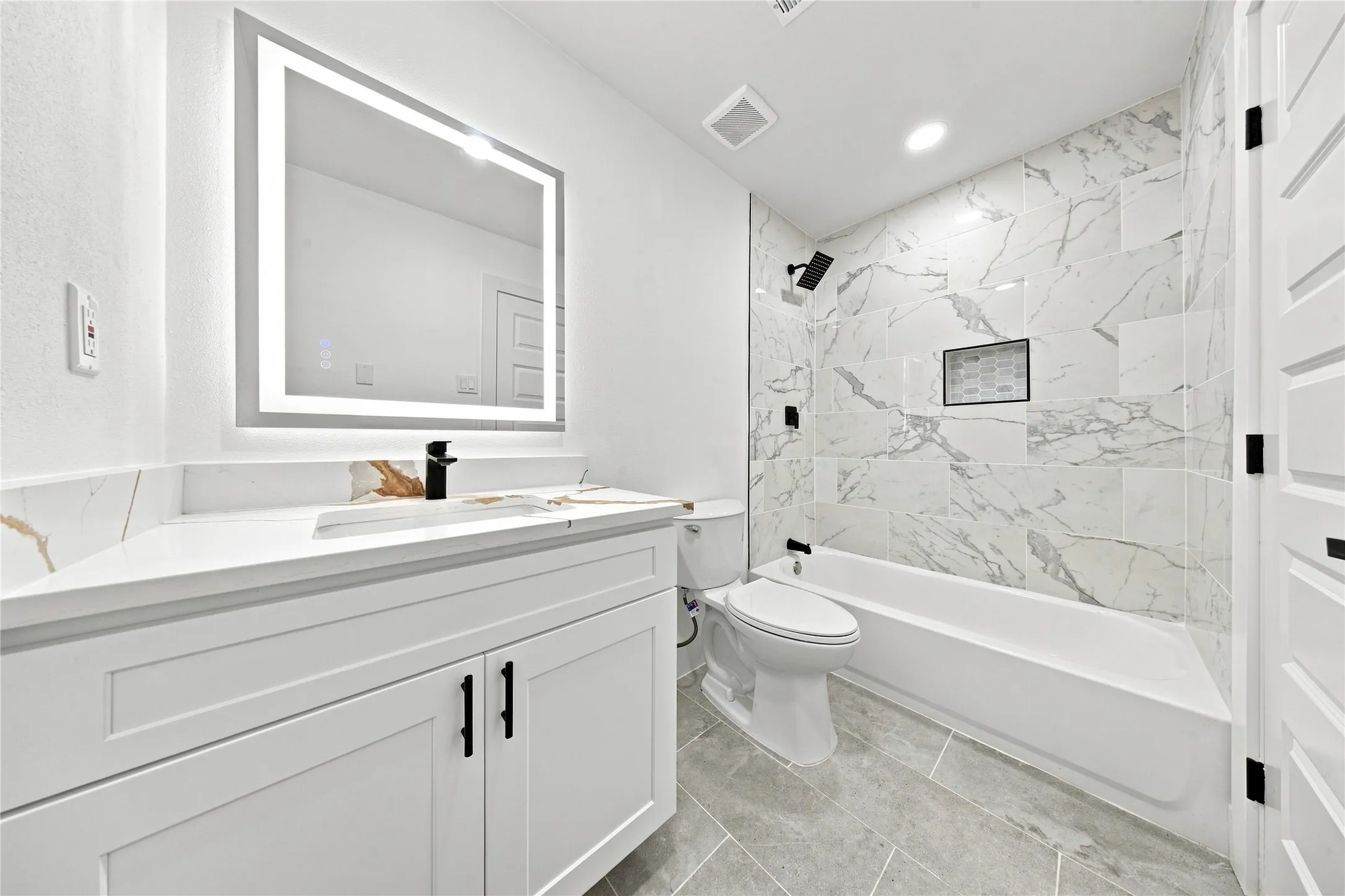 Modern vanity with integrated sink, backlit mirror, matte black fixtures, tiled shower surround, and a built-in shower niche