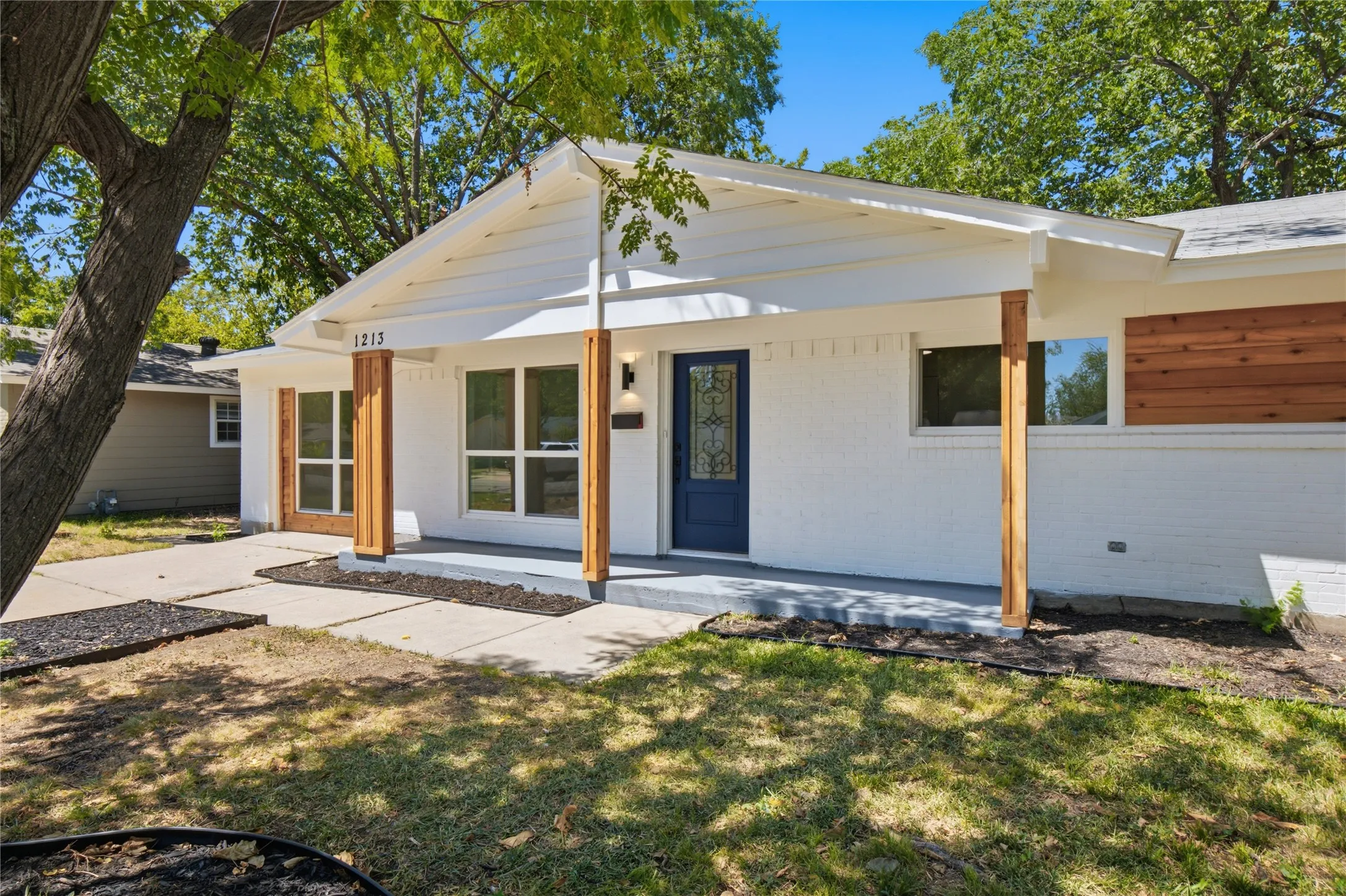 Modern ranch-style residence featuring a freshly updated exterior with clean white siding, warm wood-finish accents framing the entry, and a welcoming covered front porch