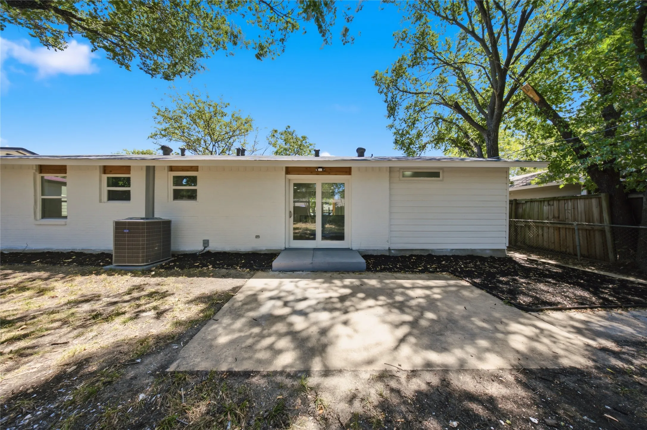 Rear exterior featuring white painted brick, horizontal siding, multiple windows, a glass-paneled door, and a concrete patio