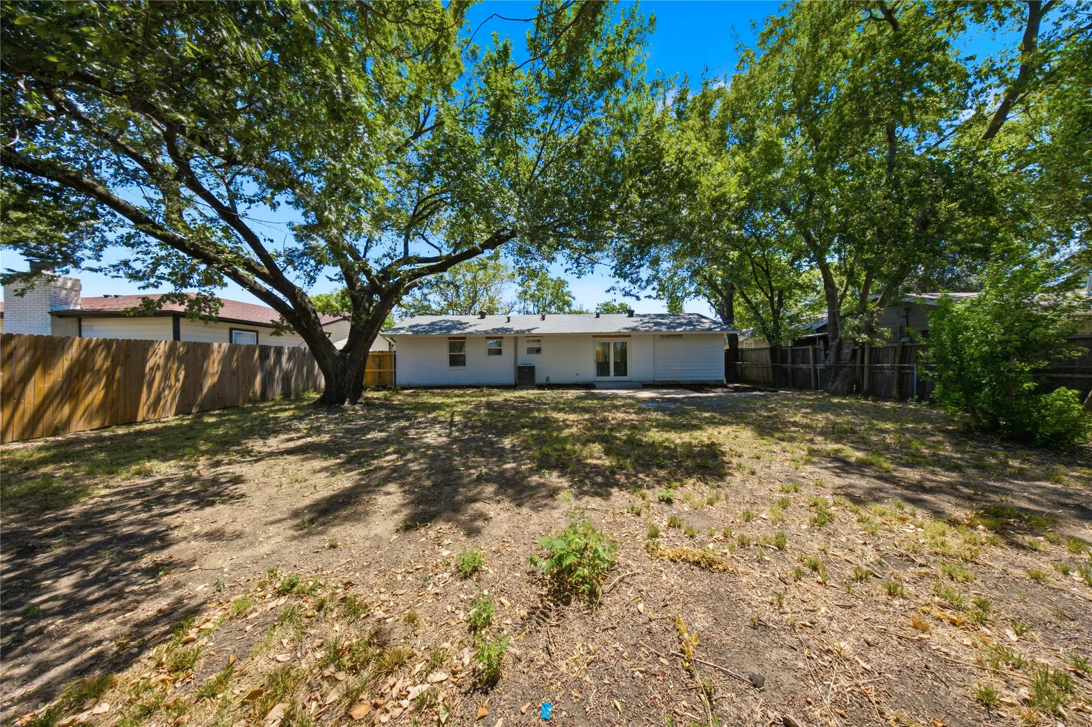 Expansive backyard featuring mature trees, a privacy fence, and a white exterior with a patio area