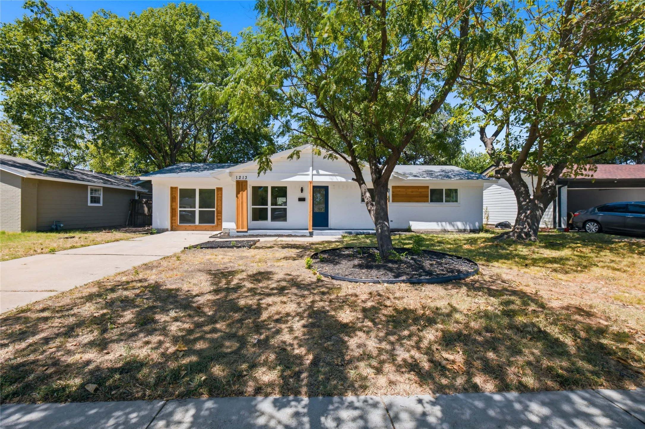 White exterior siding with a dark entry door, multiple large windows, wood-tone window accents, and a paved driveway
