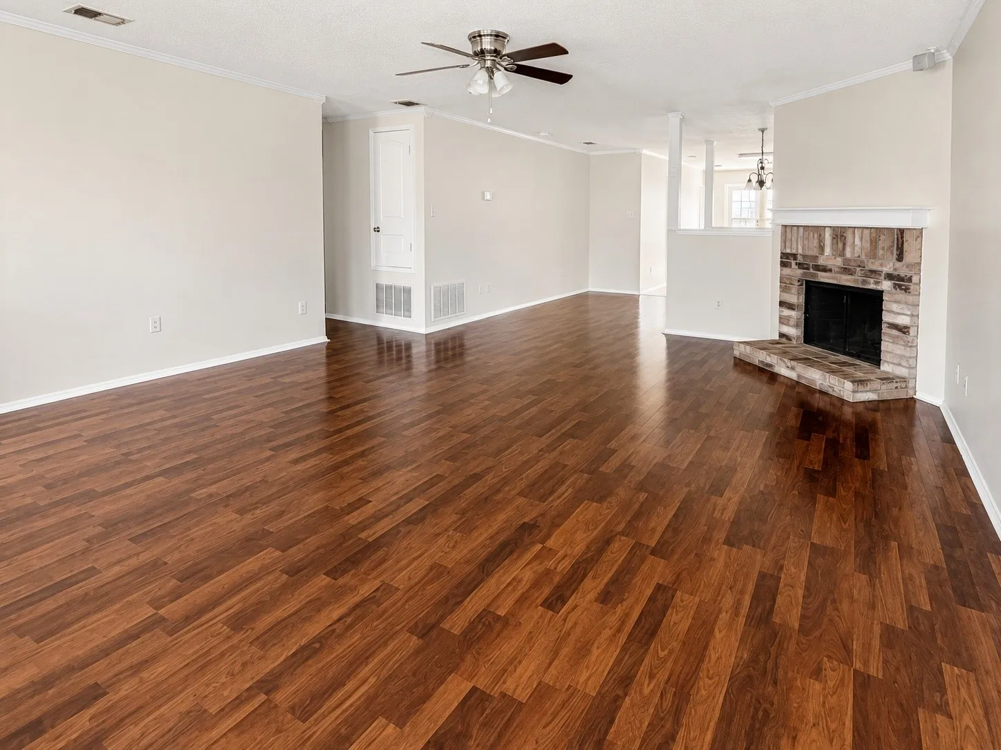 Spacious interior featuring wood-finish flooring, a ceiling fan, and a brick-finish fireplace with a hearth