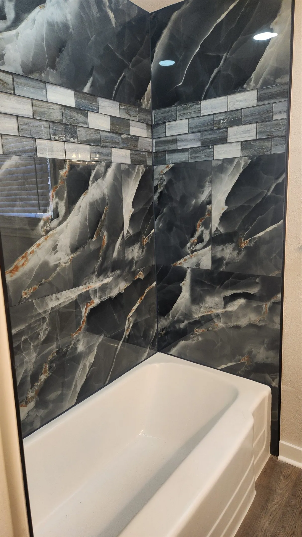 Bathtub with a large format dark tile surround featuring a lighter accent tile band