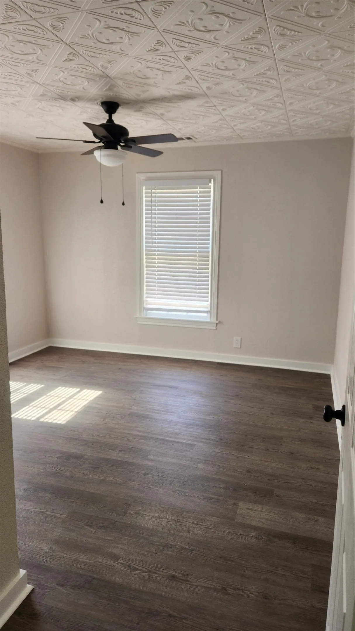 Textured ceiling with a central ceiling fan, neutral wall tones, wood-finish flooring, and a window with blinds