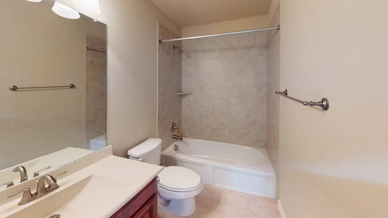 Bathroom featuring a vanity with an integrated sink, a full-width wall mirror, a tiled tub/shower combination, and ceramic tile flooring