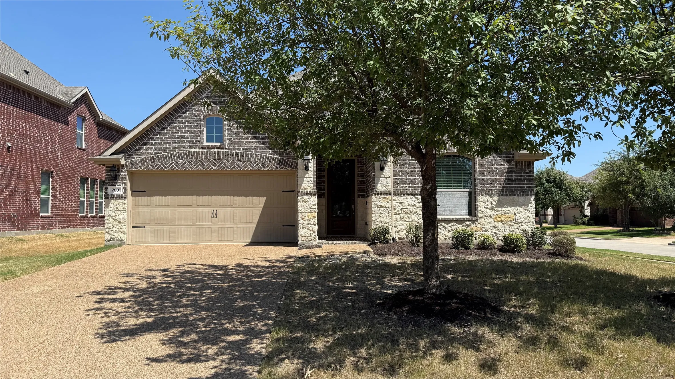 Brick and stone facade with an arched entry, prominent garage, and a manicured front lawn
