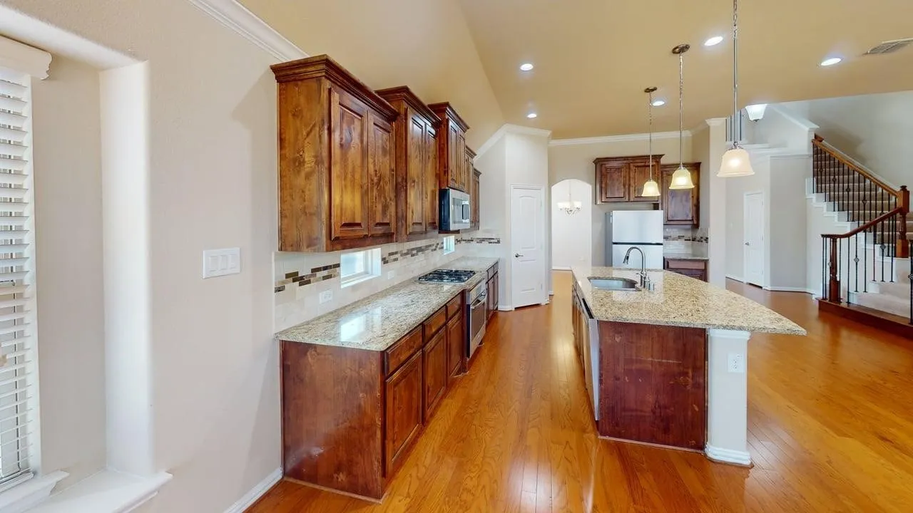 Wood-finish flooring throughout, kitchen with stone countertops, wood cabinetry, stainless steel appliances, and an island with pendant lighting