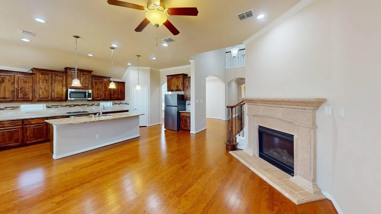 Hardwood flooring throughout, kitchen island with pendant lighting, stone fireplace, stainless steel appliances, and wood cabinetry