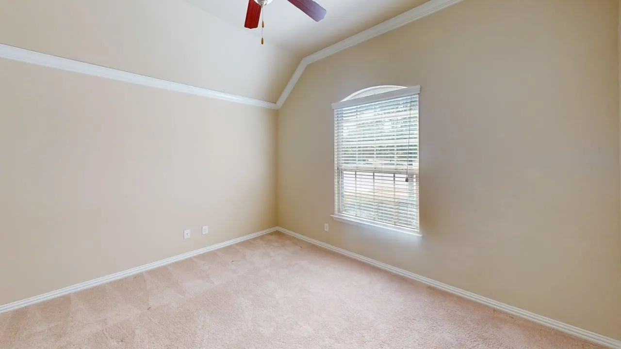 Vaulted ceiling with crown molding, ceiling fan, arched window, and neutral carpeting