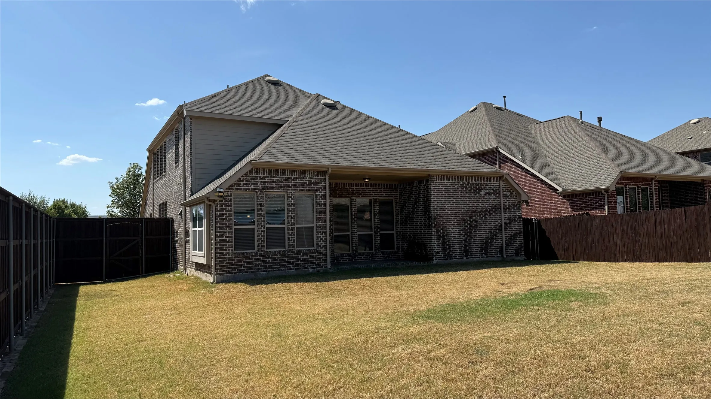 Brick exterior with a covered patio, multiple windows, and a dark wood fence enclosing the perimeter