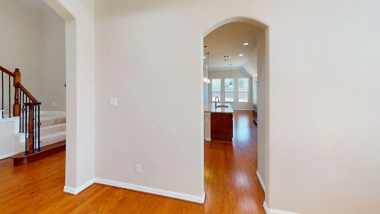Hardwood-finish flooring throughout, featuring an arched doorway and a stairway with wood and wrought iron balusters