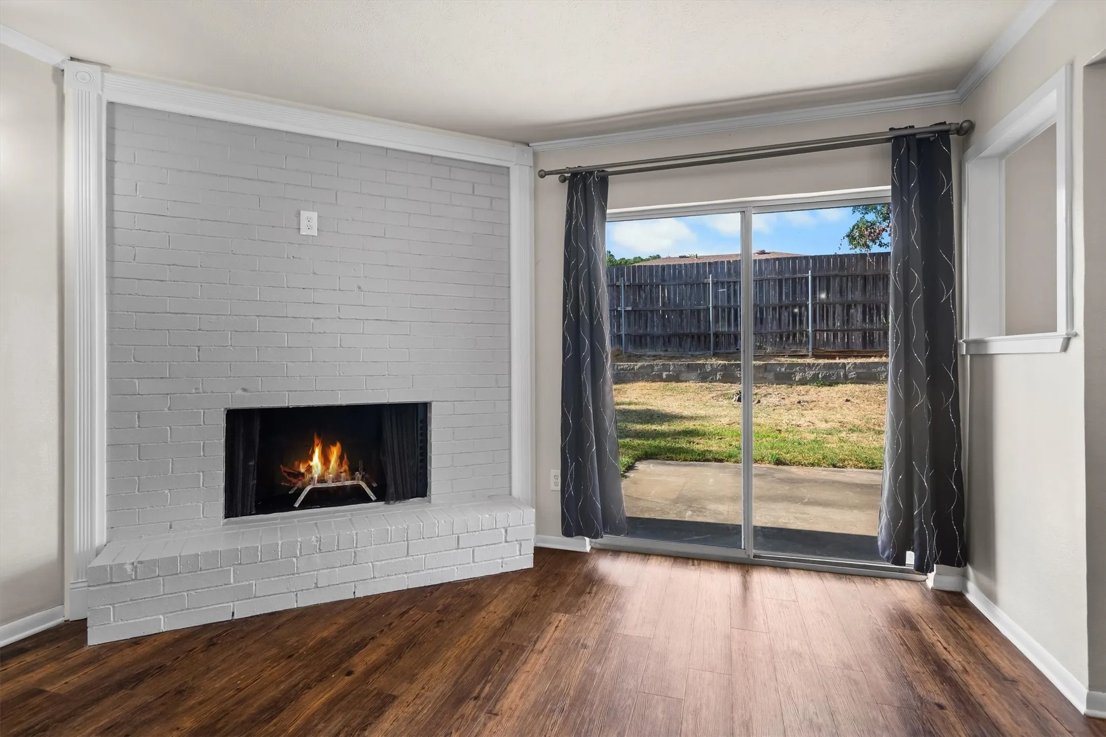 Brick fireplace with hearth, wood-look flooring, sliding glass door, and backyard patio