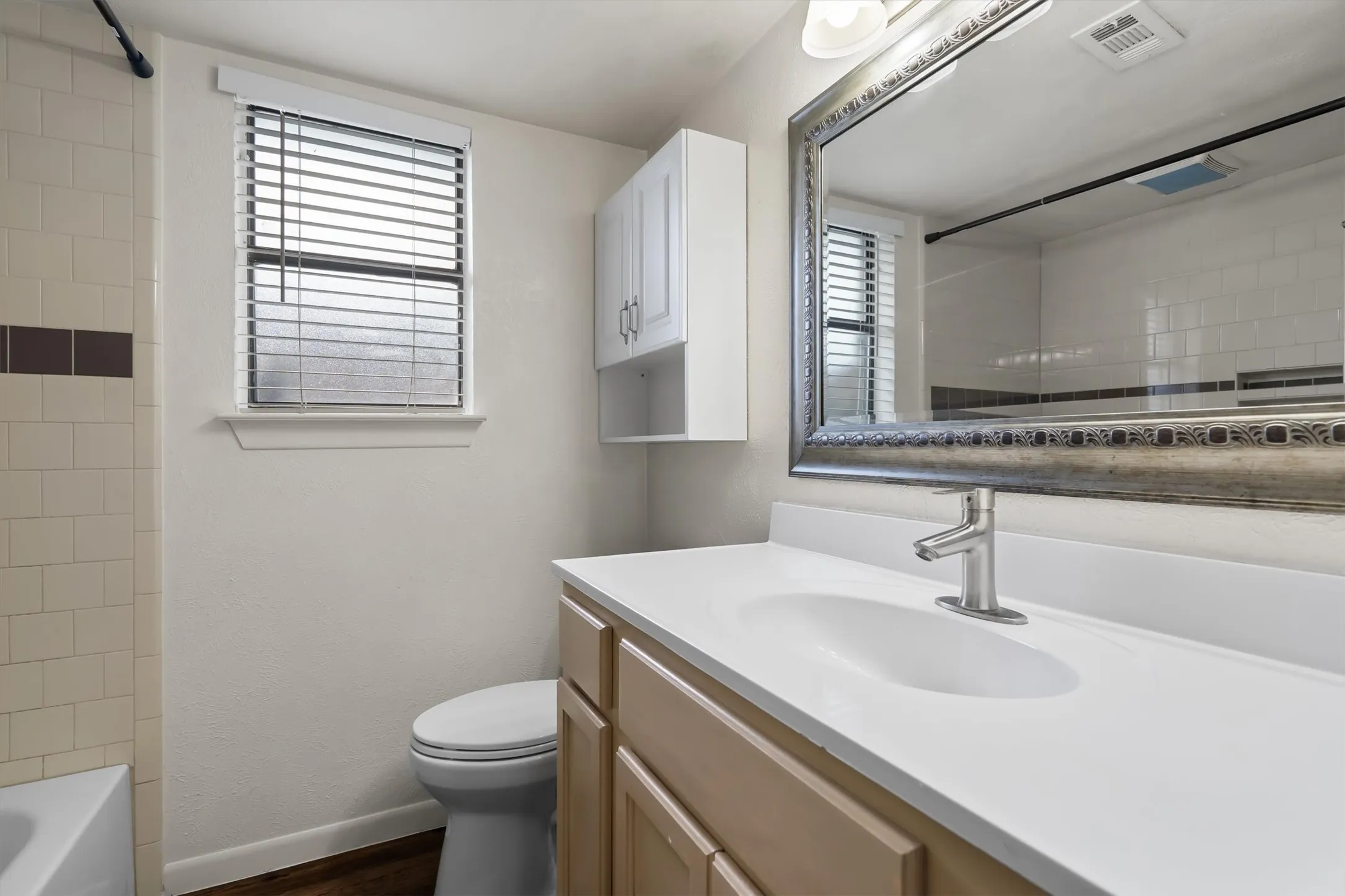Bathroom featuring a  vanity with an integrated sink, a large framed mirror, a built-in medicine cabinet, and a window with blinds