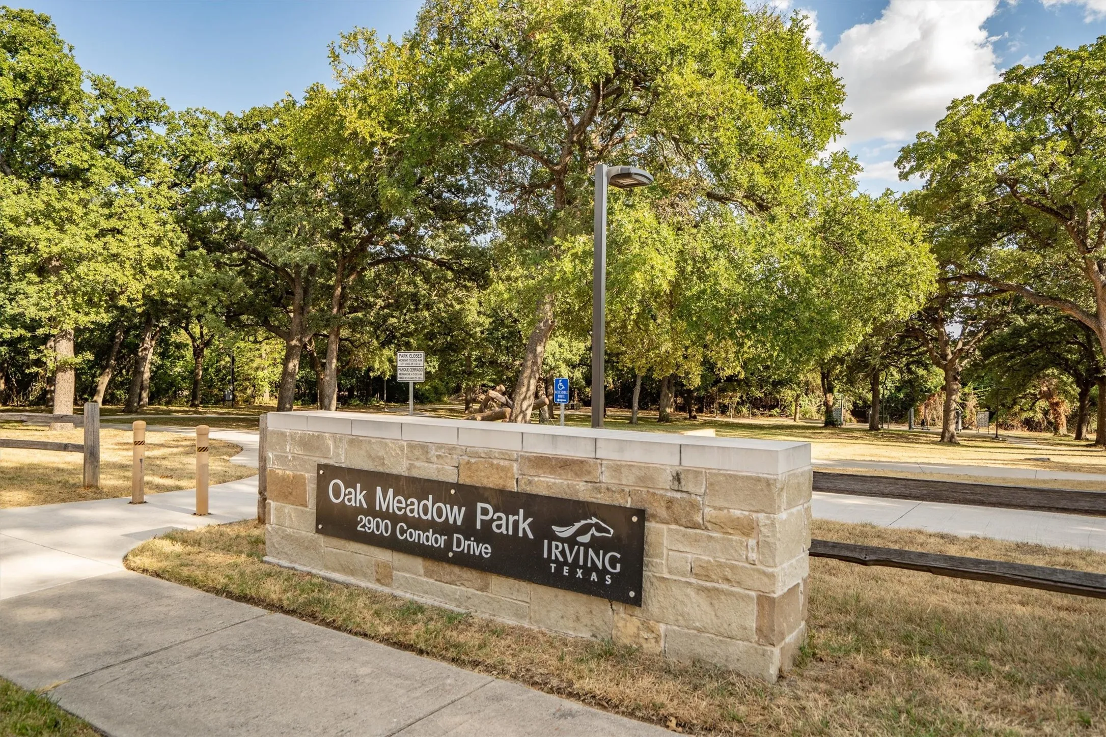 Stone and concrete park entrance with mature trees and a paved pathway