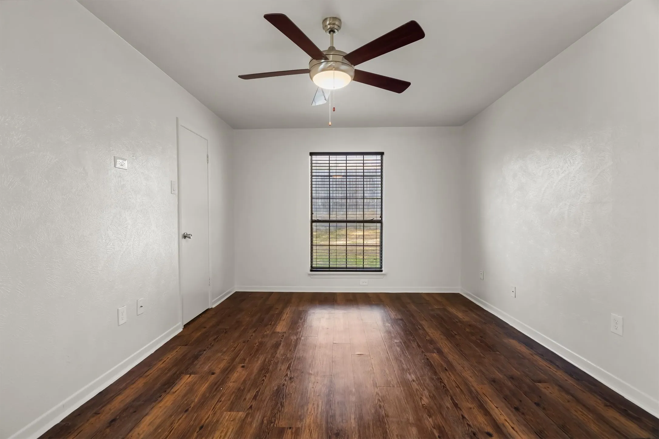 Wood-look flooring, single window with blinds, ceiling fan, white walls, and a white door