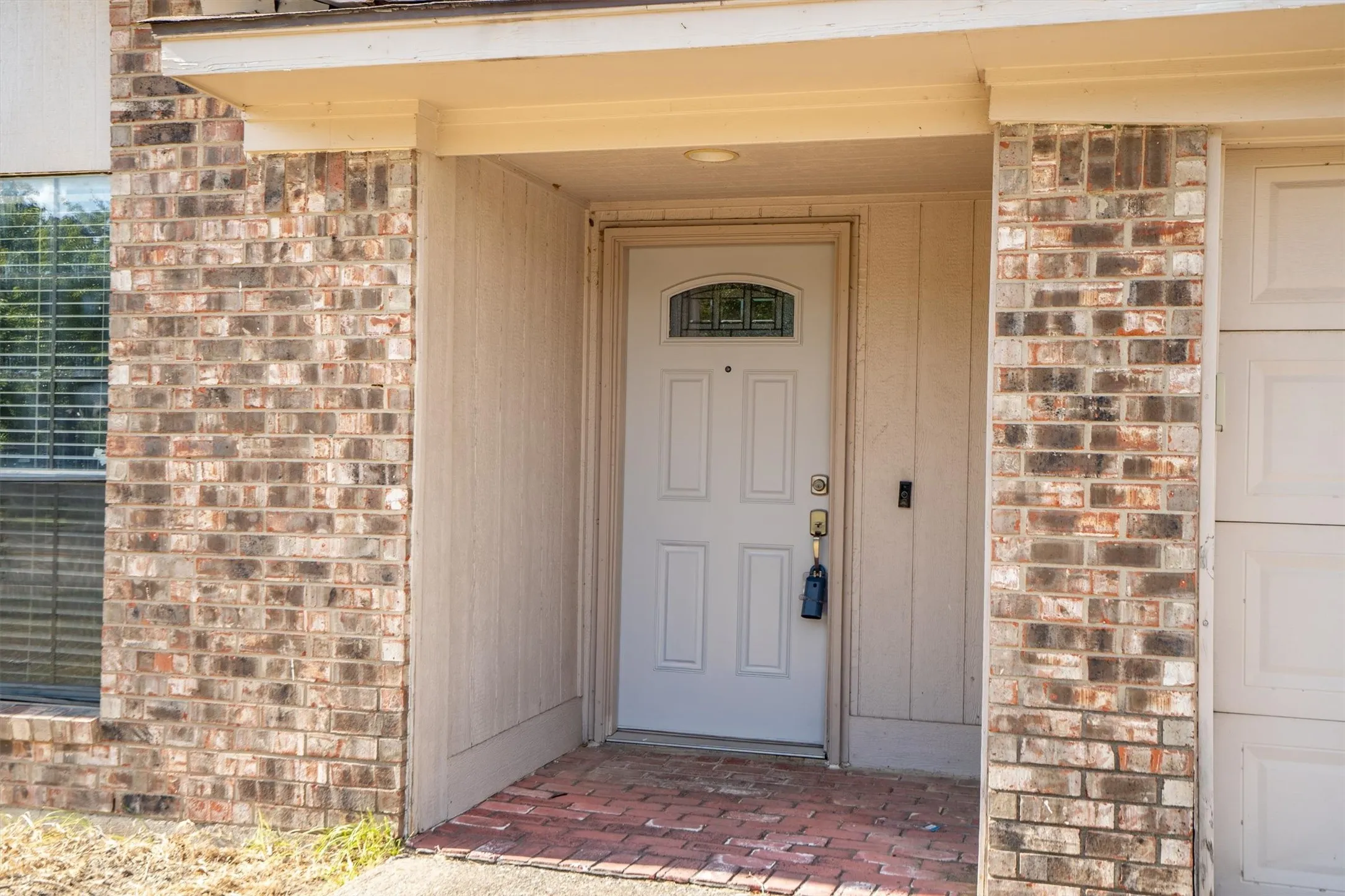 Front entry featuring a paneled door with decorative glass inlay, brick facade, covered porch, and a brick-paver threshold
