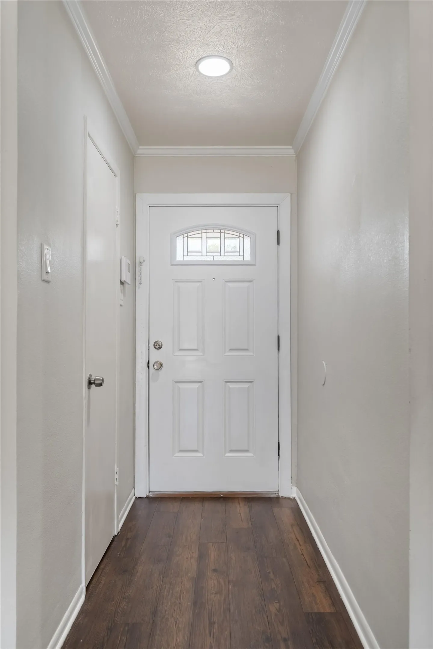 White paneled door with decorative glass insert, recessed lighting, crown molding, and wood-finish flooring