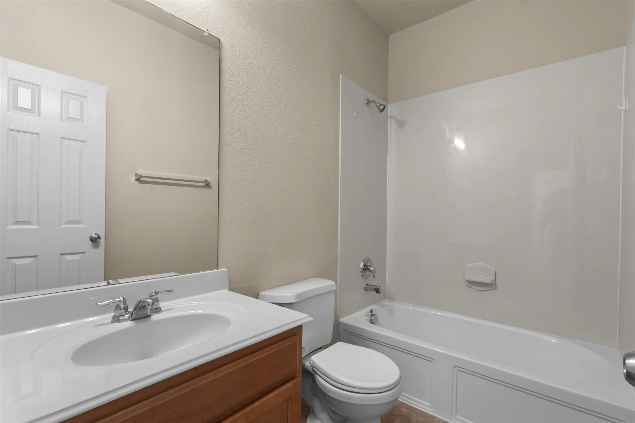 Bathroom featuring a wood-finish vanity with an integrated sink, polished chrome fixtures, a full-width mirror, and a shower-tub combination with a white surround