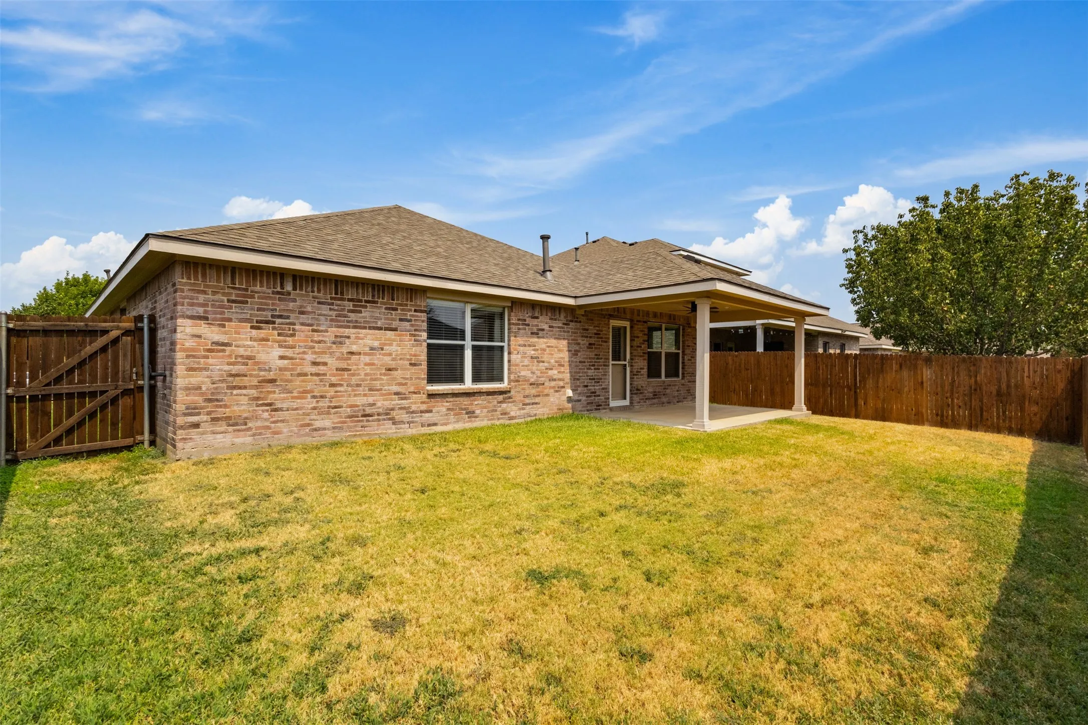 Brick exterior with covered patio, concrete slab, and wood privacy fencing
