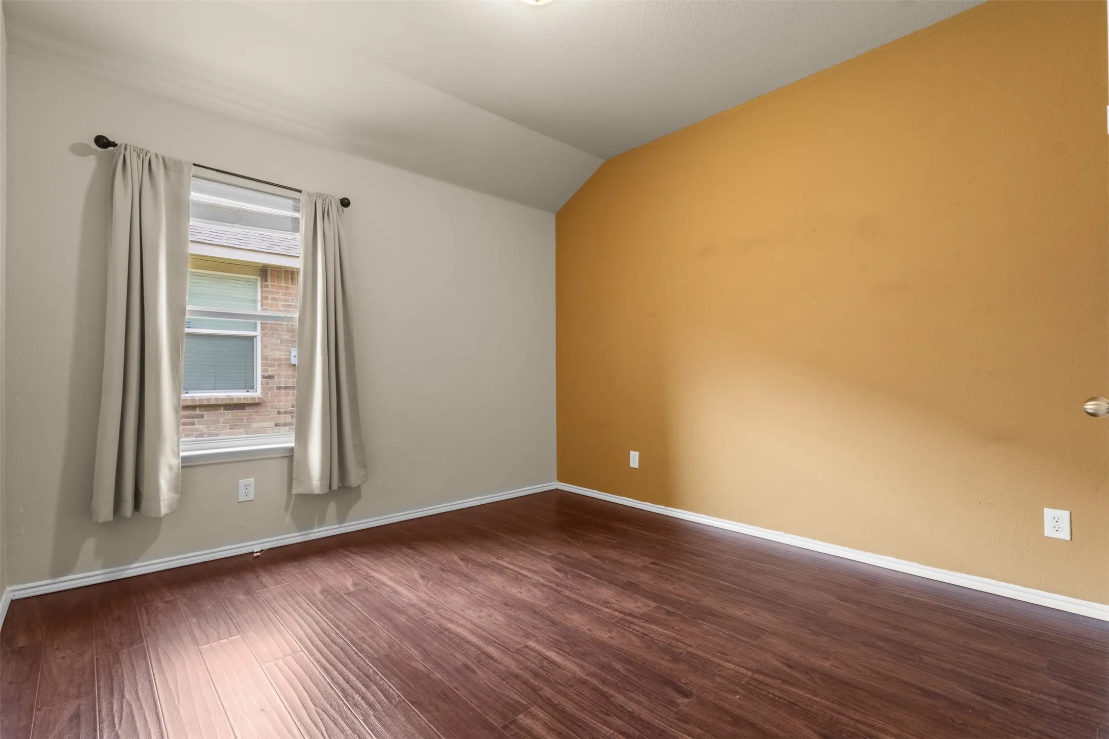 Wood-finish flooring, vaulted ceiling, and neutral wall tones complement the bright window