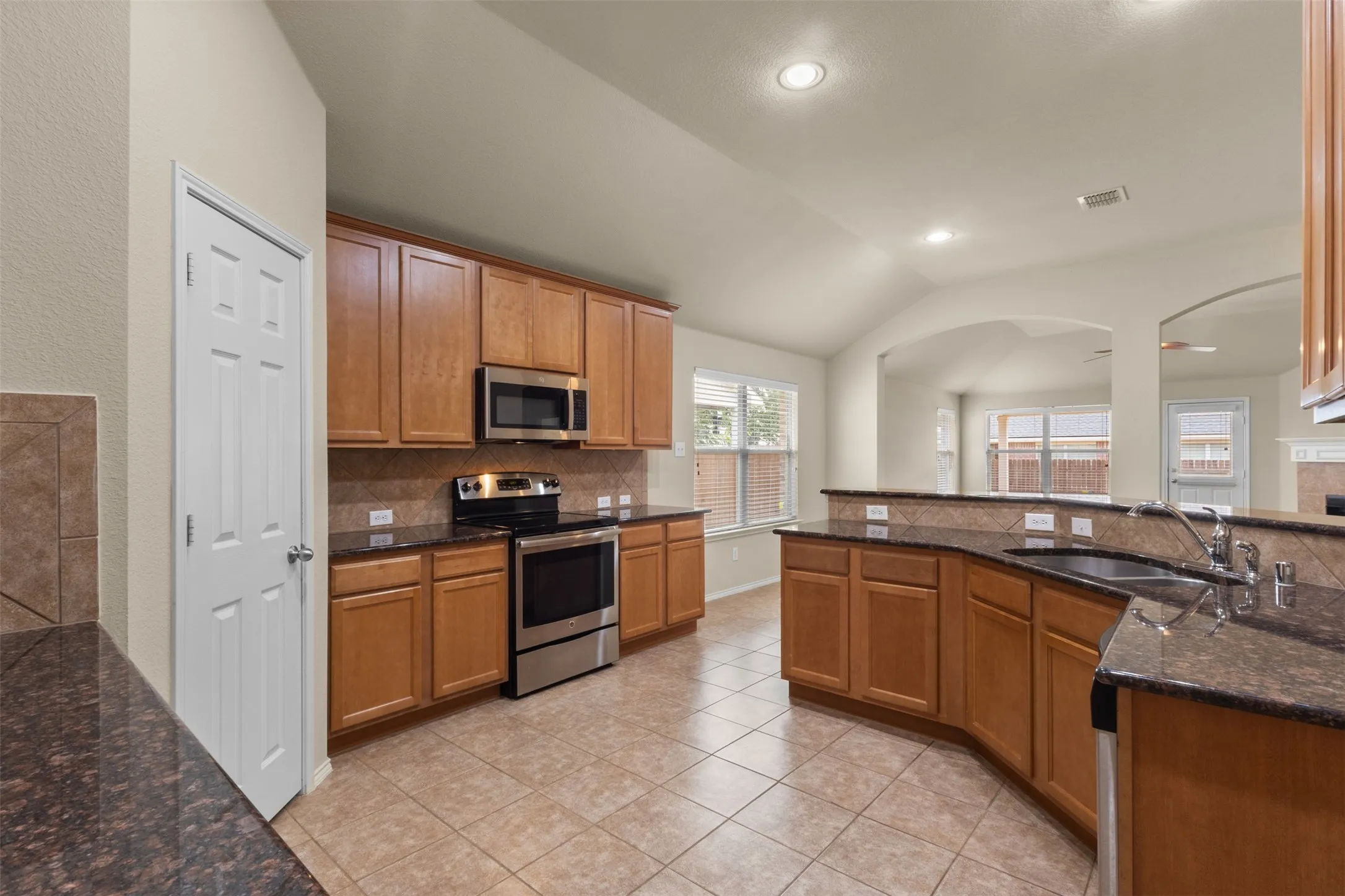 Kitchen featuring wood cabinetry, dark countertops, stainless steel appliances, tile flooring, and recessed lighting