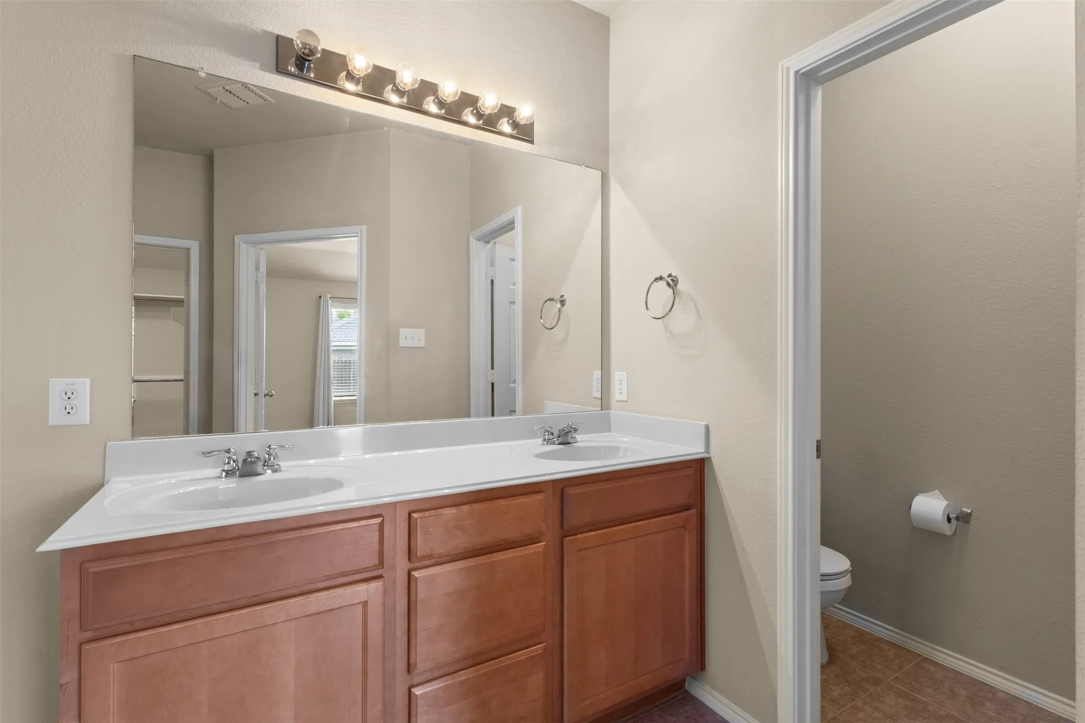 Double vanity with integrated sinks, wood-finish cabinetry, and a chrome light fixture