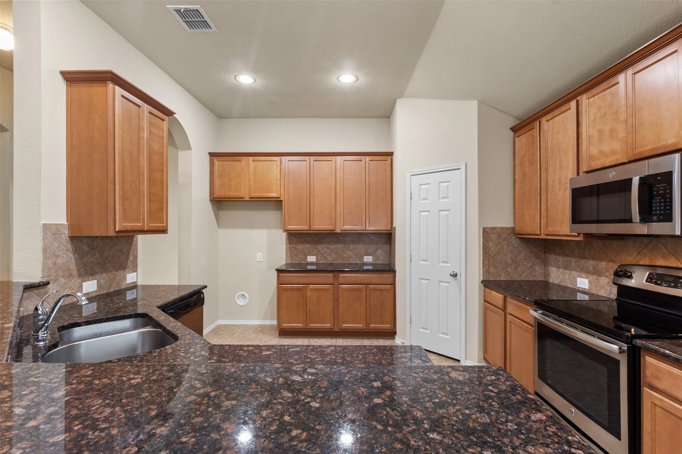 Spacious kitchen featuring warm wood-finish cabinetry, granite countertops with breakfast bar seating, stainless steel appliances including double wall ovens, and recessed lighting throughout