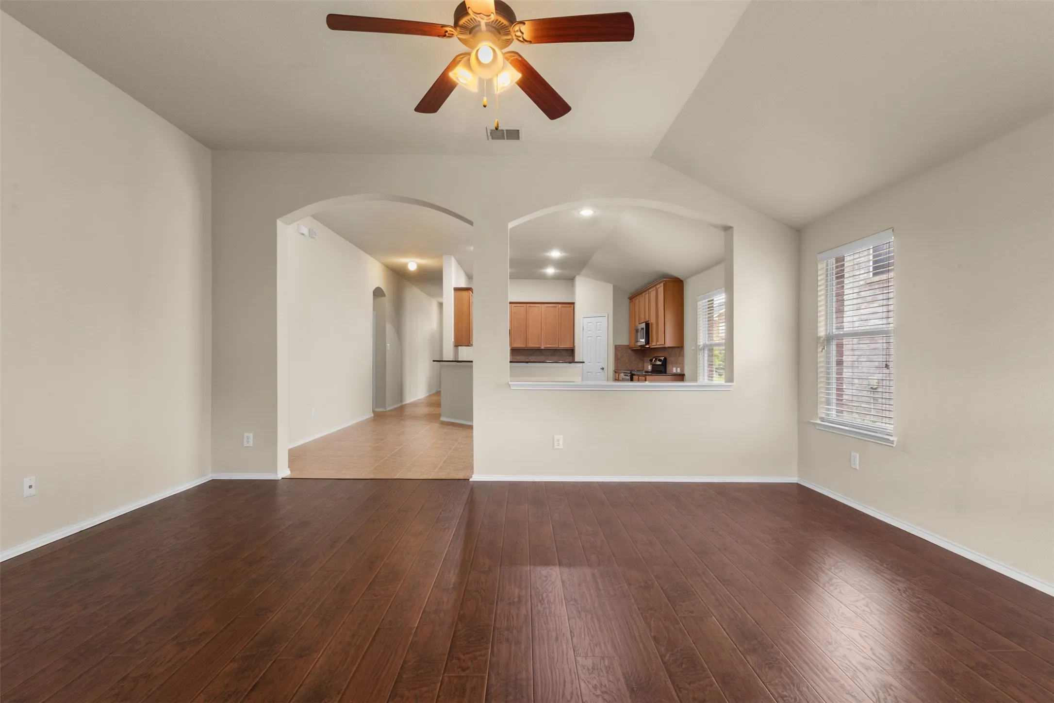 Vaulted ceiling with a ceiling fan, wood-finish flooring, and arched doorways