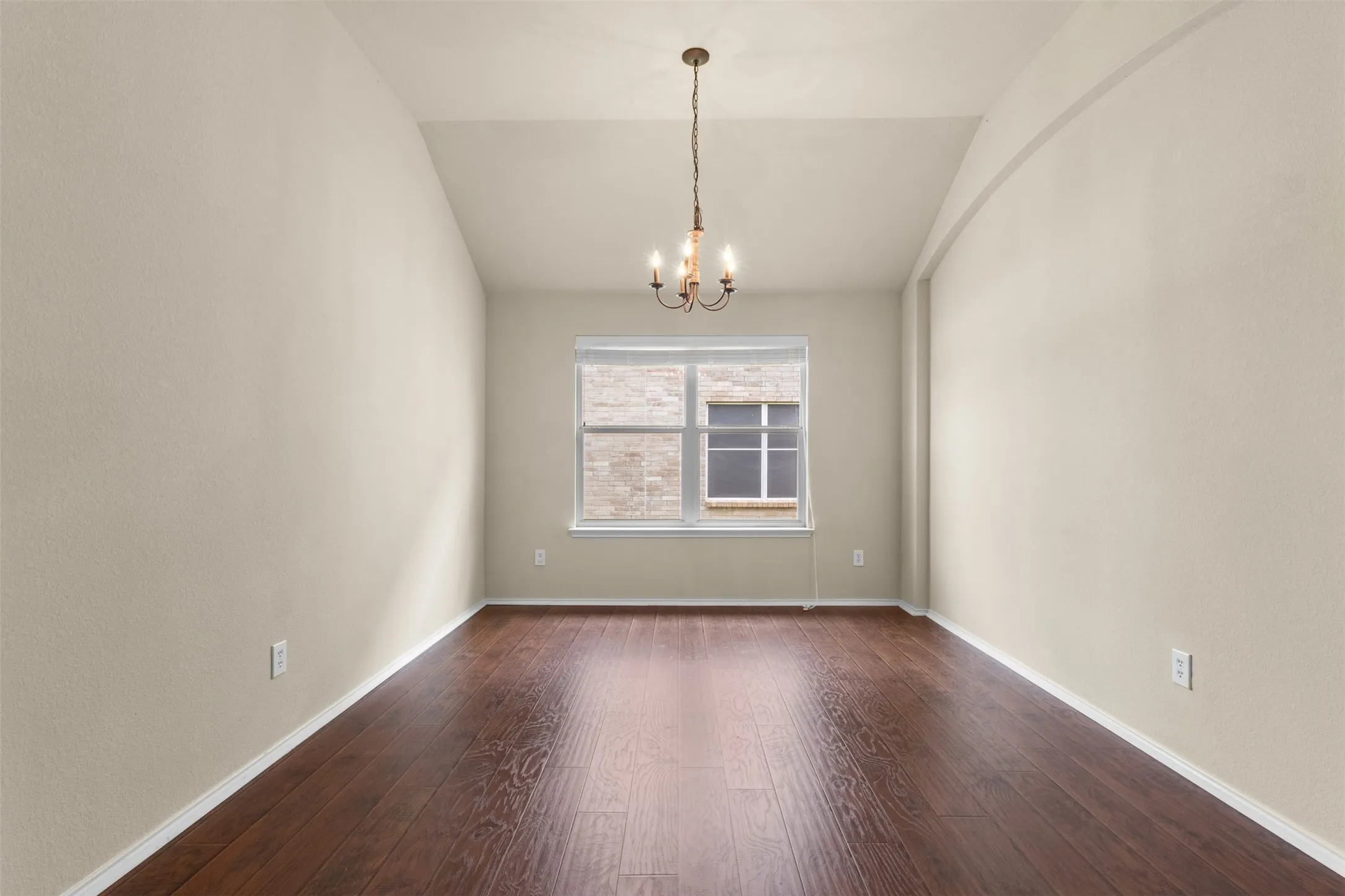 Vaulted ceiling with chandelier lighting, wood-finish flooring, and a window with blinds