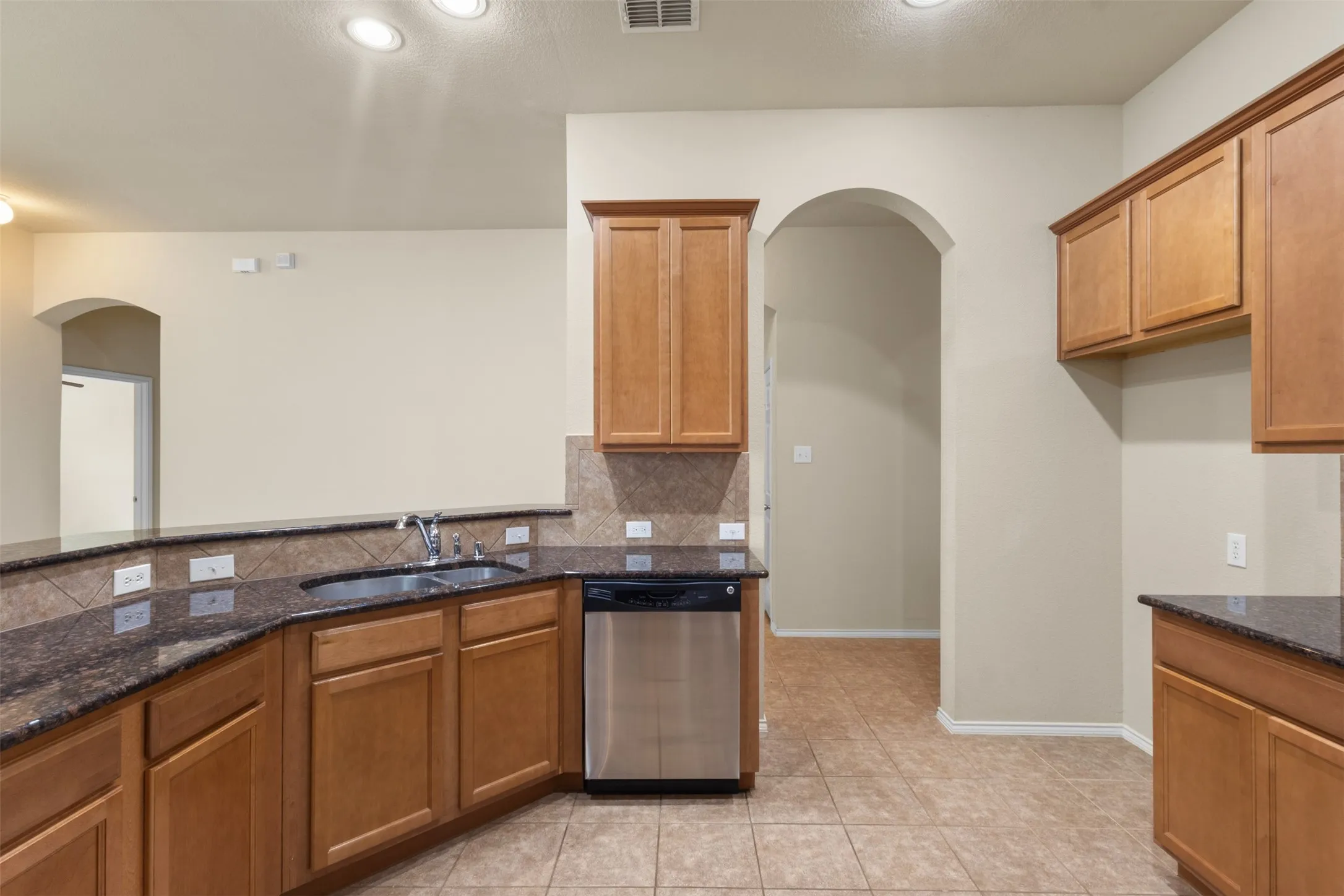 Kitchen featuring wood cabinetry, dark stone countertops, tile backsplash, and tile flooring