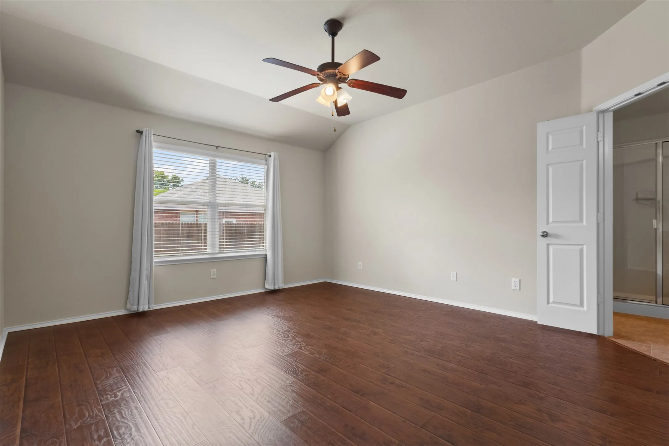 Wood-finish flooring, vaulted ceiling, ceiling fan with integrated lighting, window with blinds, and paneled interior door