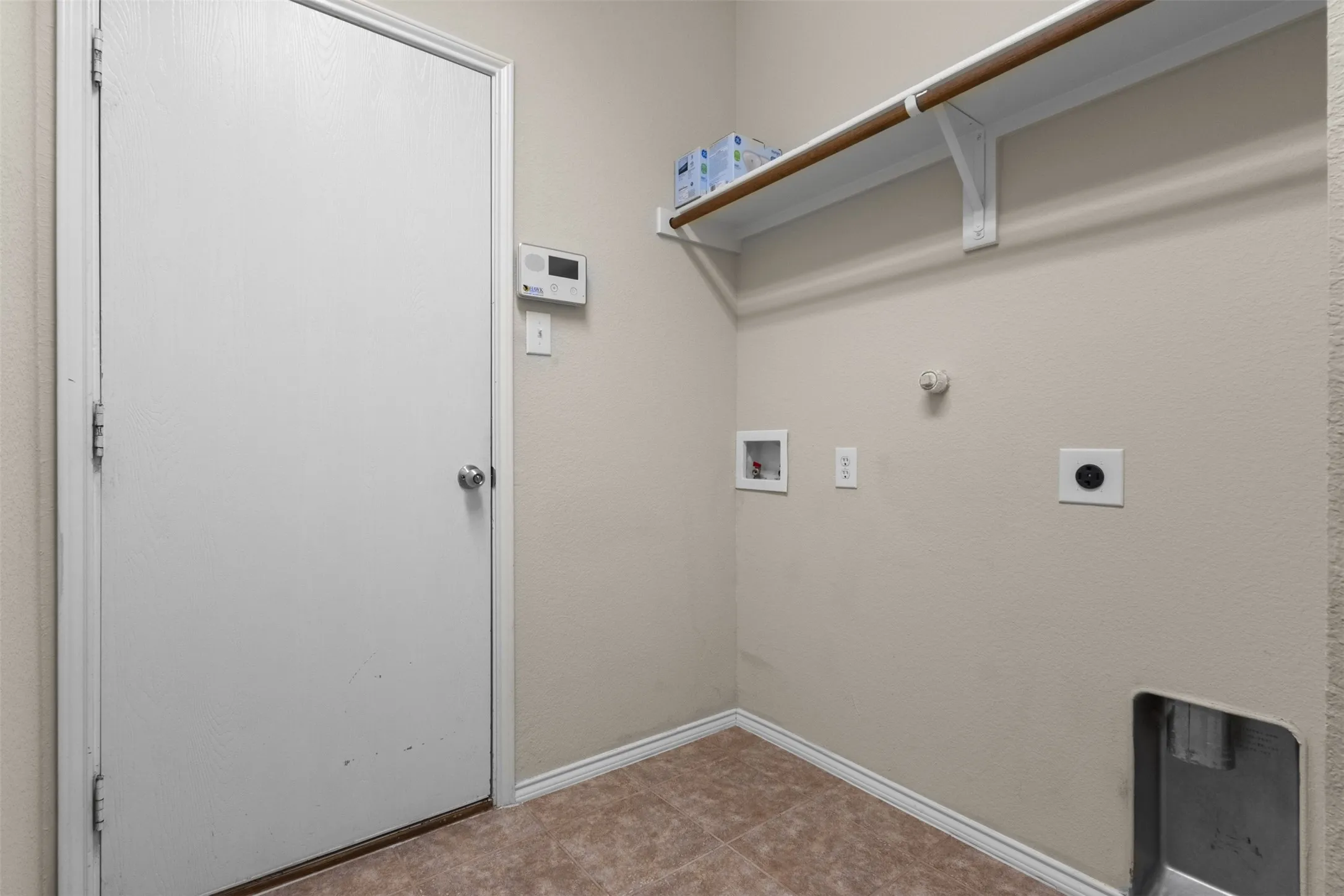 Laundry area featuring tile flooring, neutral wall tones, and an upper storage shelf with a hanging rod