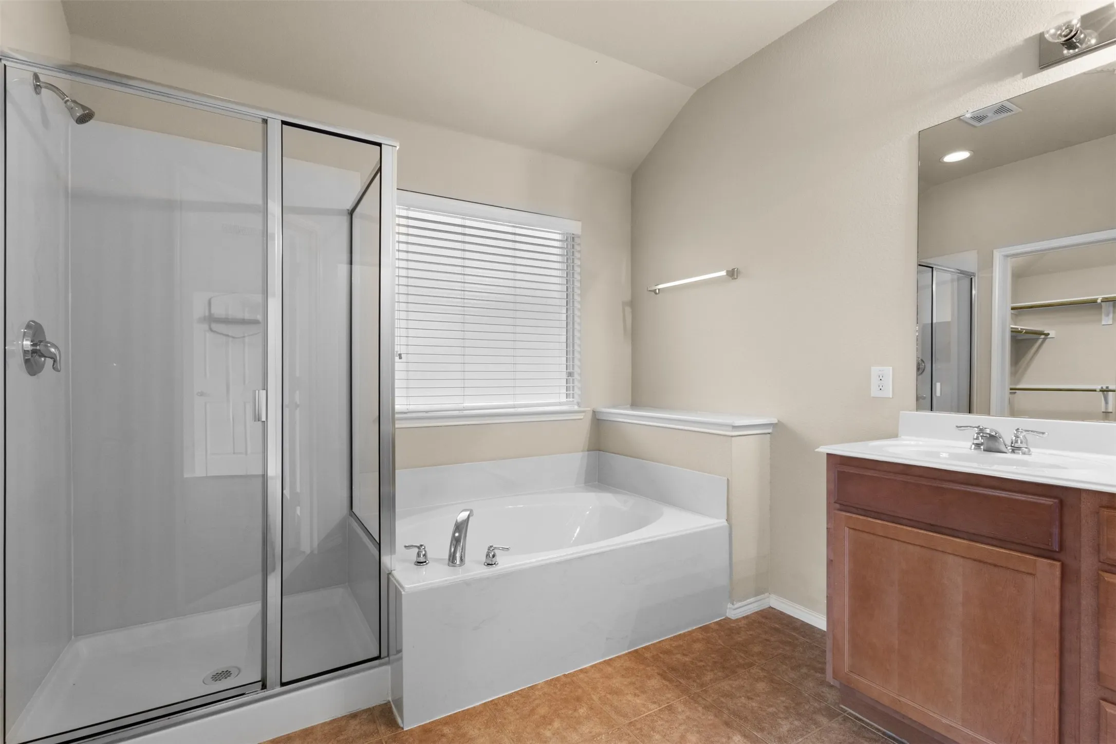 Tile flooring, glass-enclosed shower, soaking tub, window with blinds, and a vanity with an integrated sink