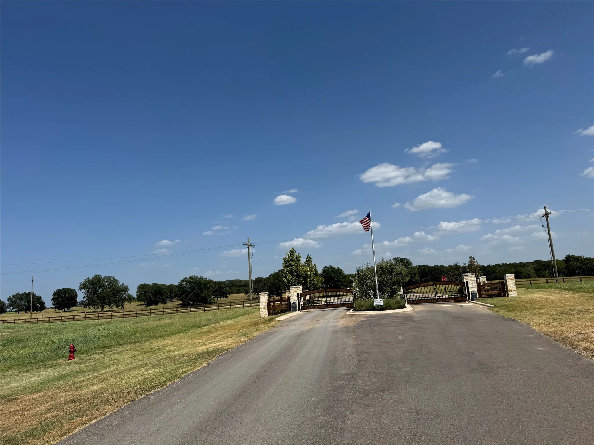 Gated entry with stone pillars, wood fencing, and mature trees