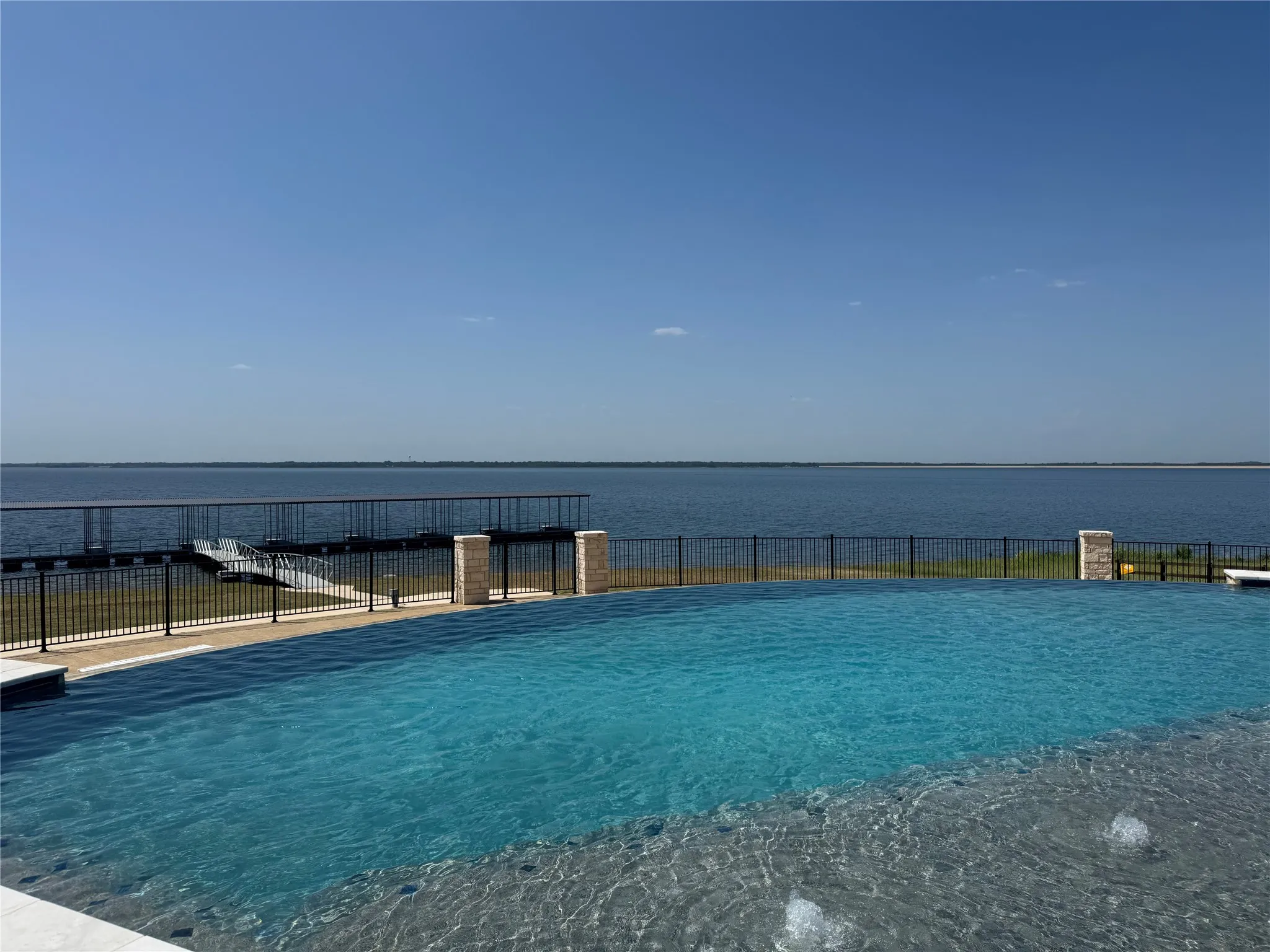 Infinity-edge pool with integrated spa, bordered by a wrought iron fence and stone pillars