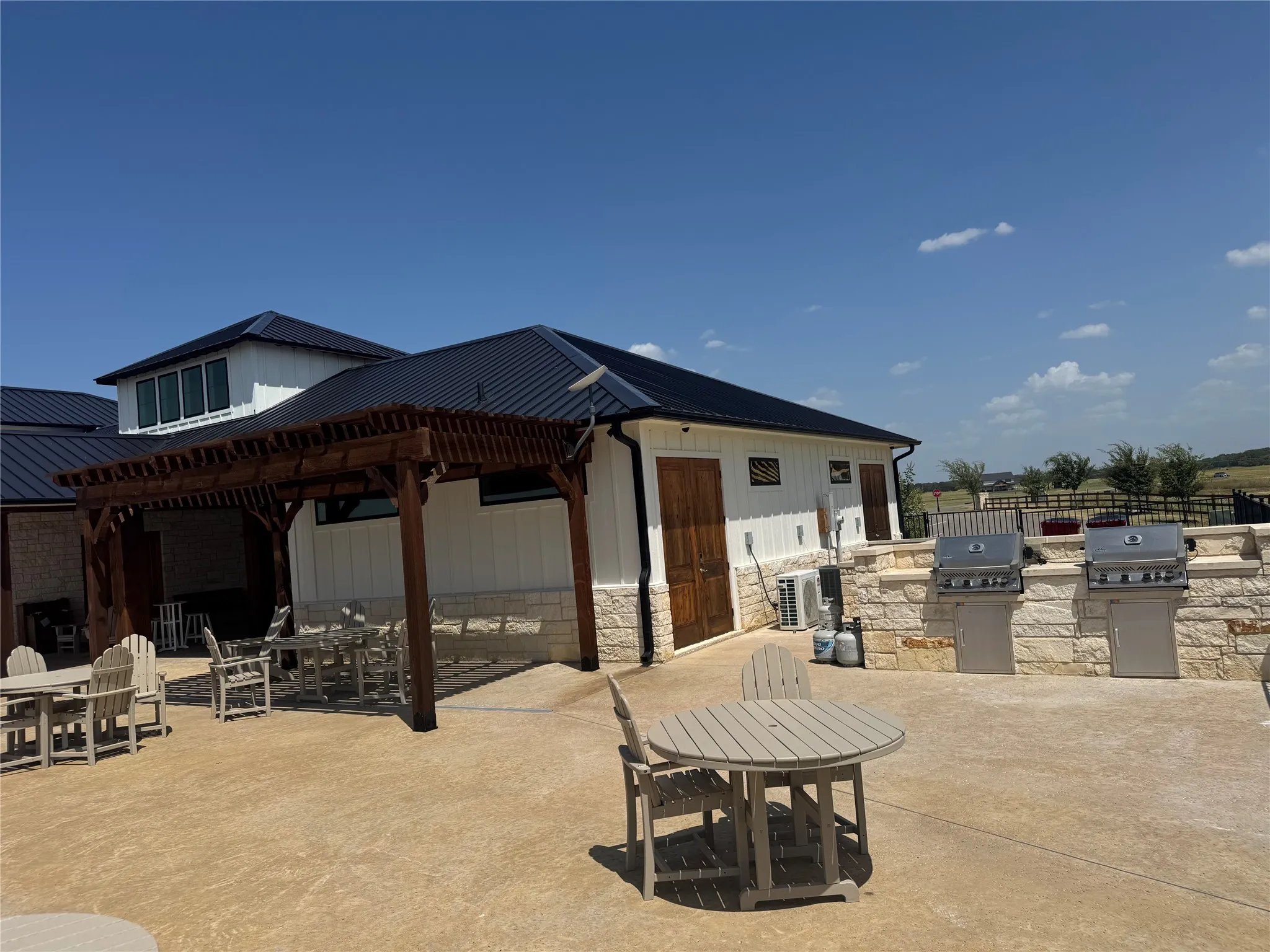 Expansive outdoor patio with a wooden pergola and built-in stone outdoor kitchen featuring two grills