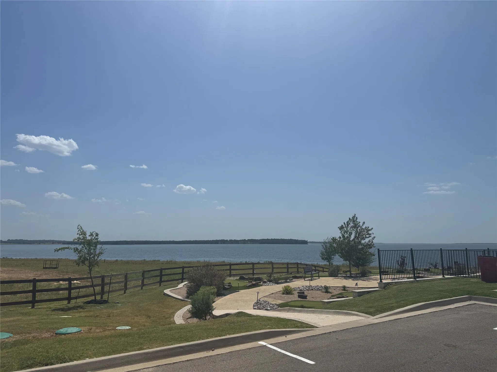 Expansive waterfront property featuring a paved walkway, mature landscaping, and a secure perimeter fence