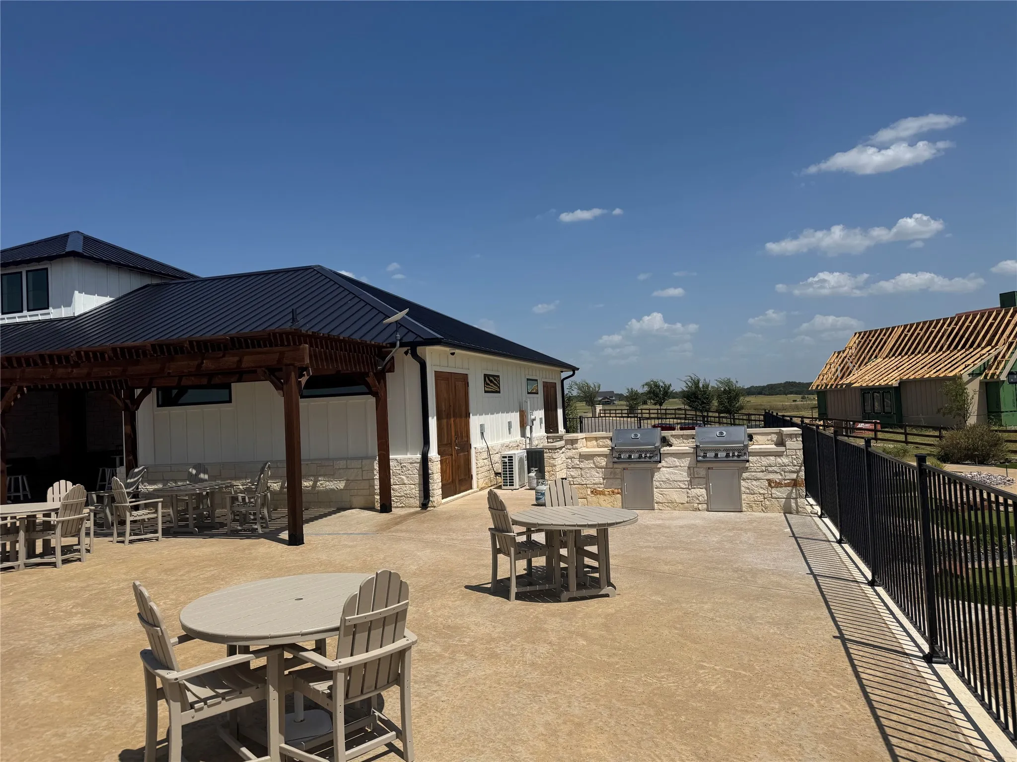 Expansive outdoor patio featuring a pergola, built-in outdoor kitchen with two grills, and a black metal fence